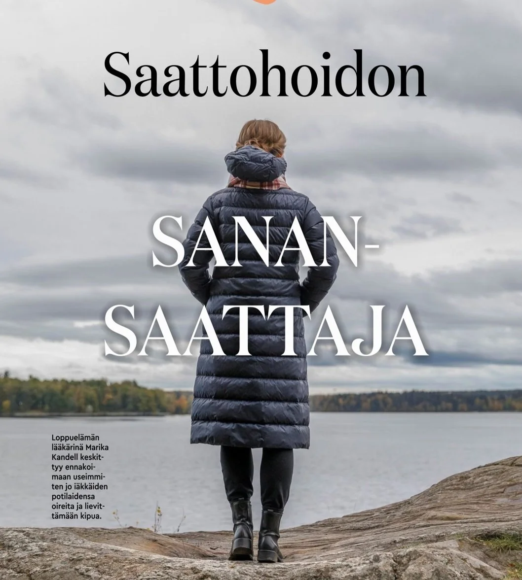 Nainen katsoo järvelle ja kauas pilviseen taivaalle, pukeutuneena paksuun takkiin ja saappaisiin.