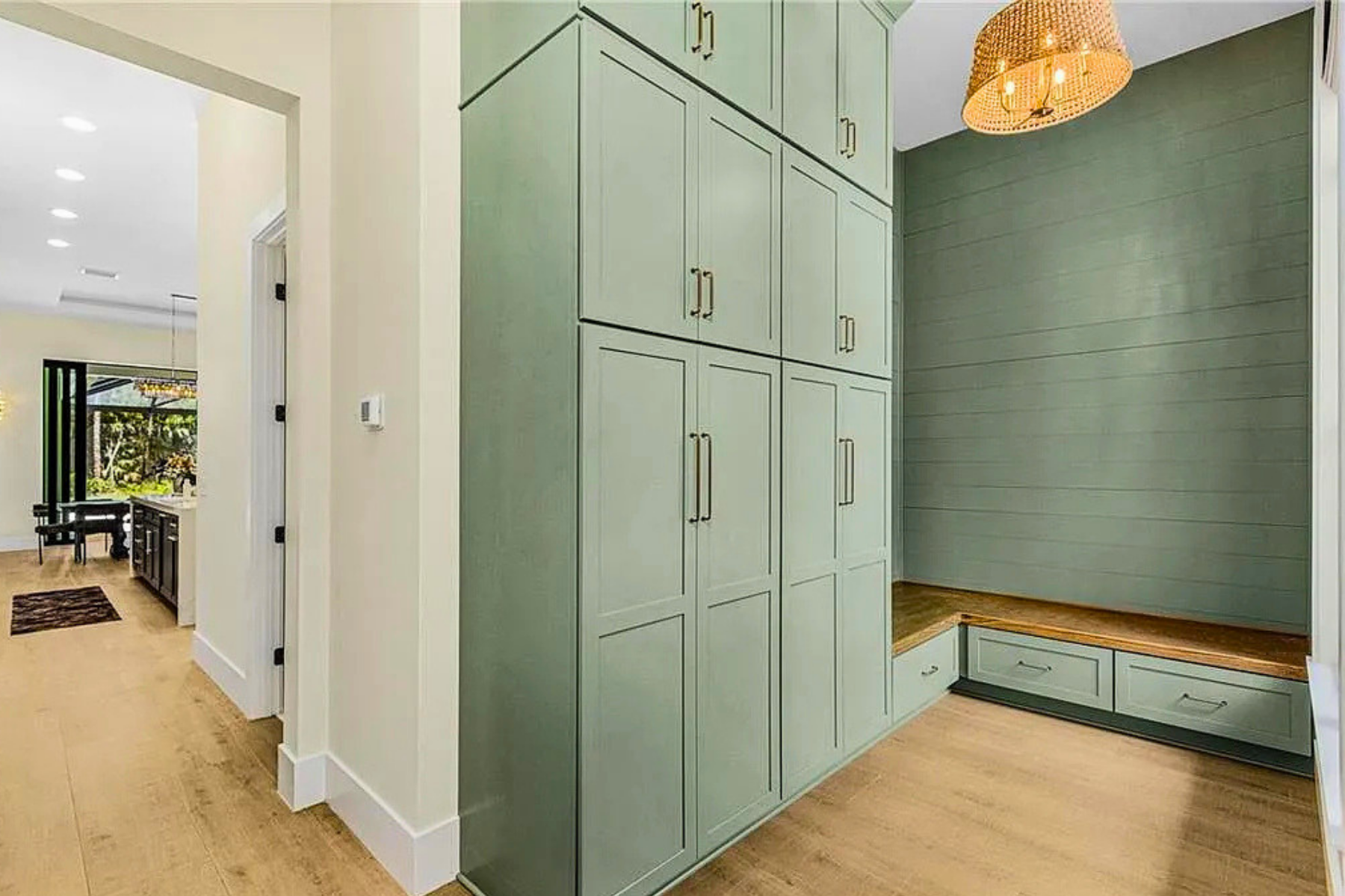 A built-in green storage unit with cabinets and drawers in a contemporary kitchen or entryway, with a wooden bench and light wood flooring.