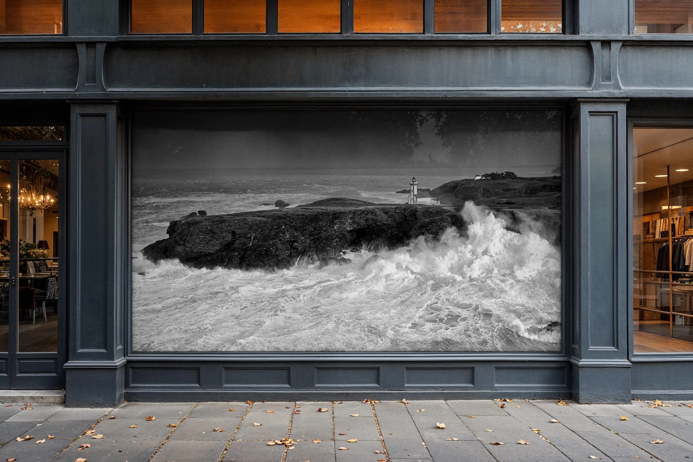 Photo d'une fenêtre avec une scène en noir et blanc d'une mer agitée et un phare sur une roche dans l'océan.