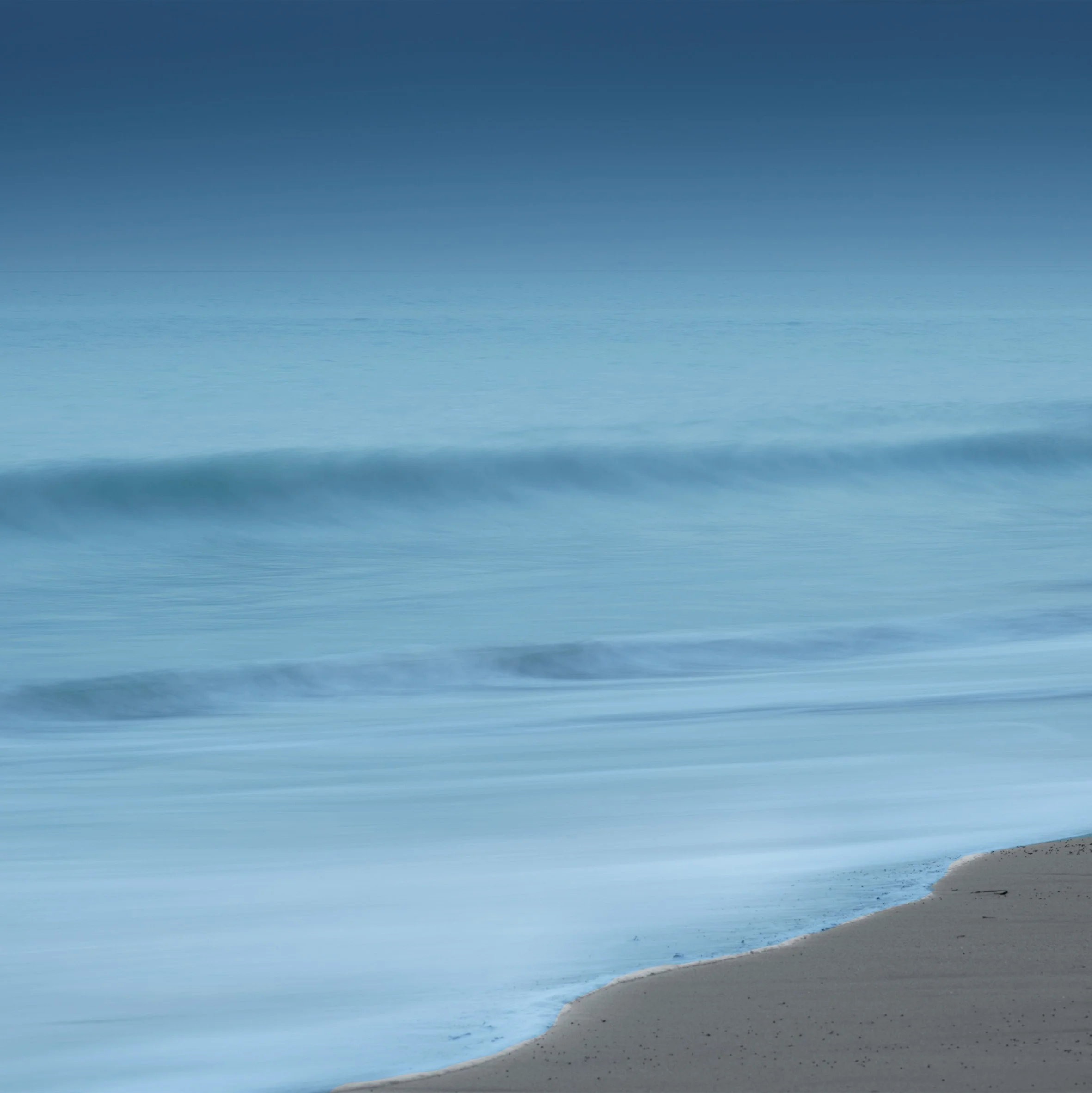 Plage de sable avec eaux calmes et horizon dégagé, ciel clair sans nuages.