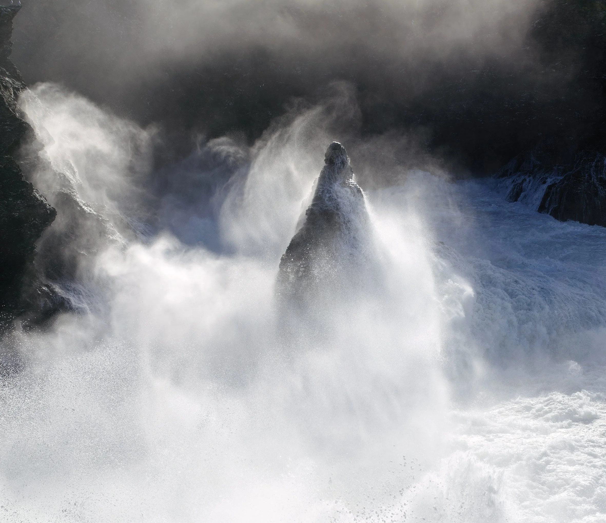 Vague d'eau de mer éclaboussant contre des rochers au lever du soleil, créant une brume.