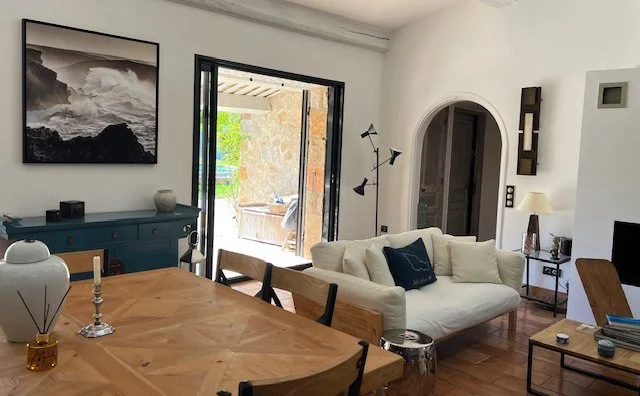 Salon avec canapé blanc, table en bois, et porte-fenêtre donnant sur une terrasse extérieure