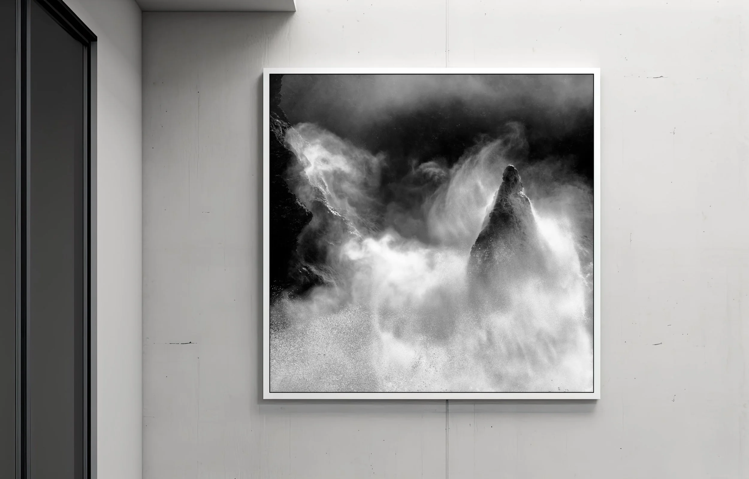 Une œuvre d'art en noir et blanc représentant des vagues déchaînées sur la mer, encadrée et affichée sur un mur blanc dans un espace d'exposition.