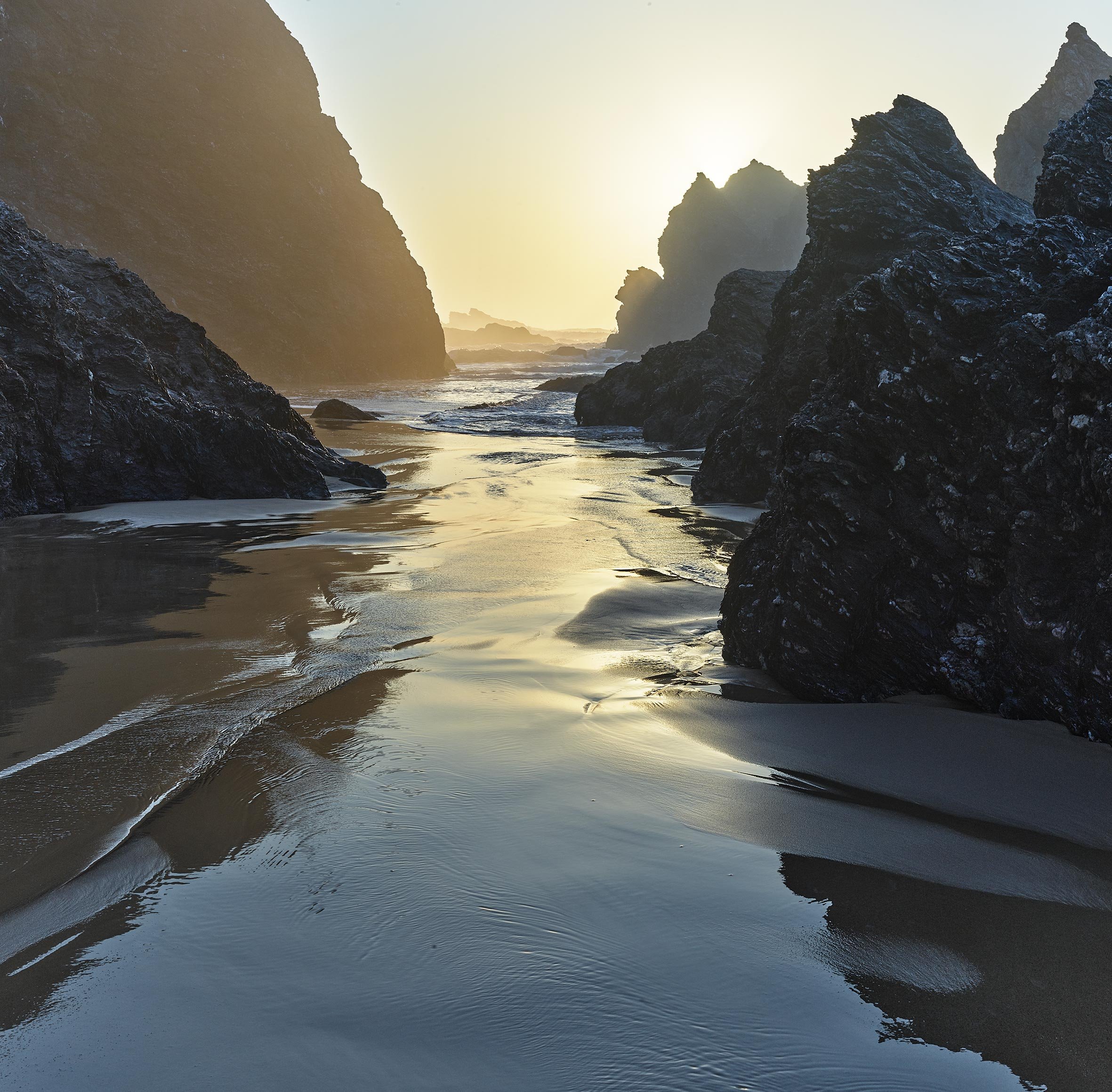Paysage côtier avec des rochers escarpés entourant une mer calme au coucher du soleil.