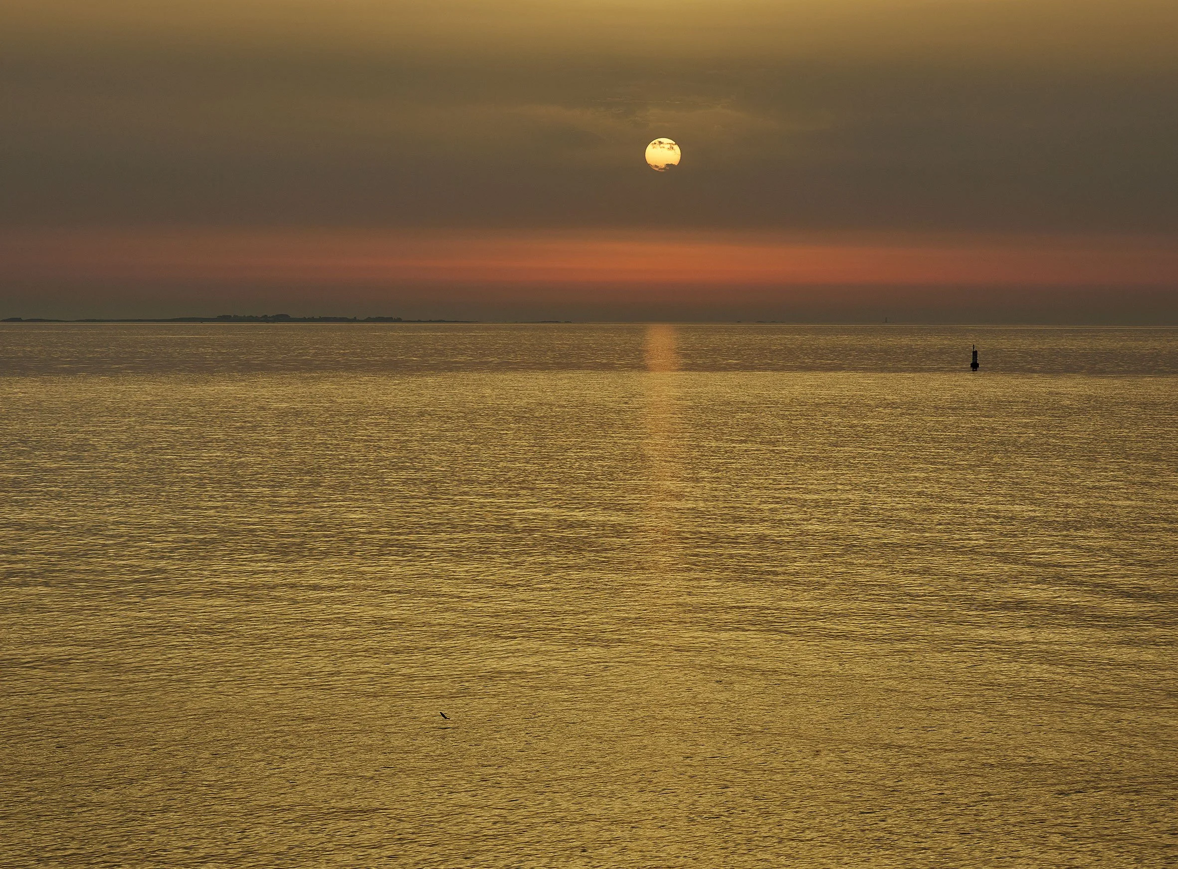 Le soleil dans le ciel, reflété sur une étendue d'eau calme, avec un horizon lointain et un bouée flottante à droite.