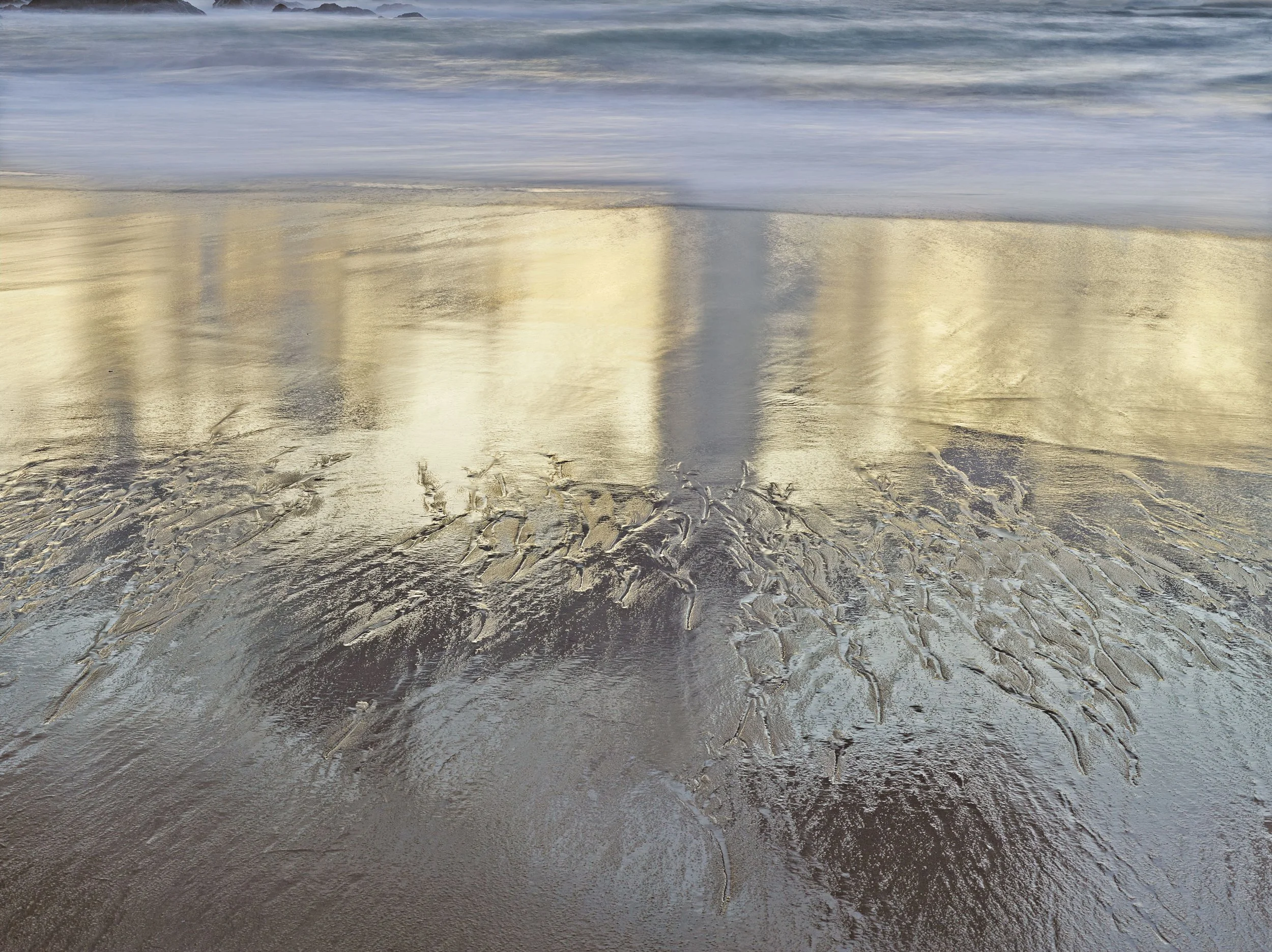 Plage de sable avec des formations de glace à la surface, avec la mer en arrière-plan et un ciel nuageux.