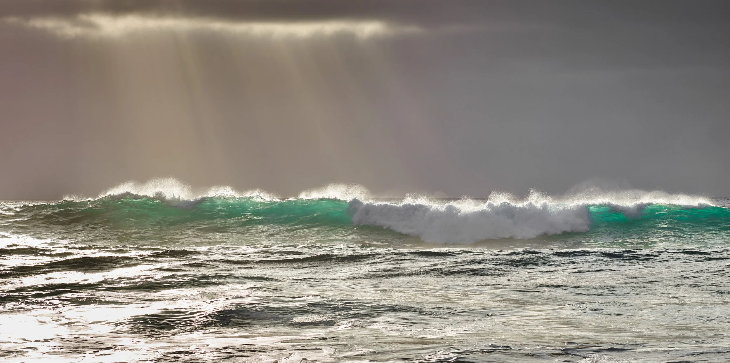 Vagues déferlantes en mer sous un ciel sombre avec des rayons de lumière perçant à travers les nuages.