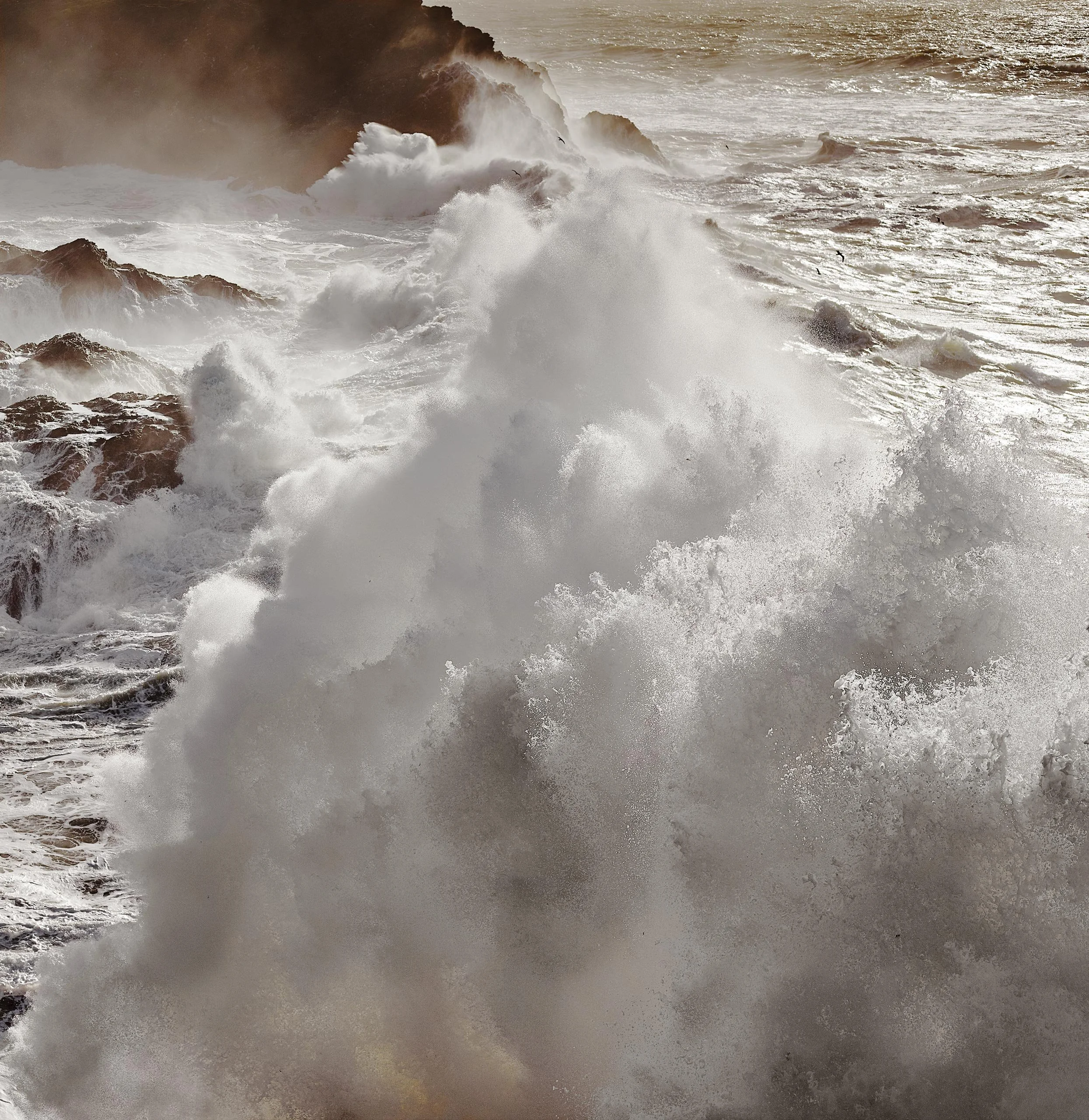 Vagues déchaînées de l'océan Atlantique, éclaboussures sur des rochers, ciel brumeux.