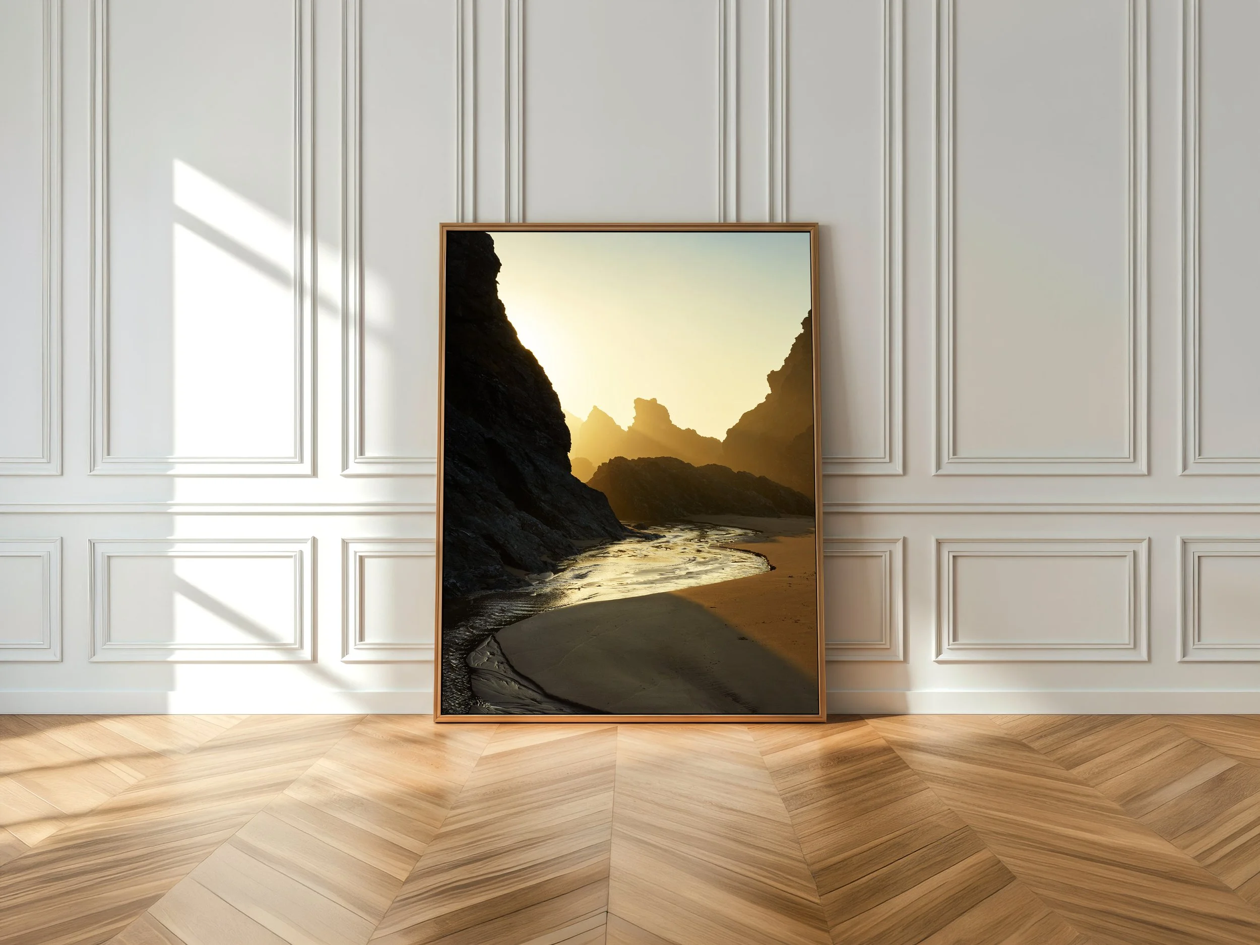 Un tableau représentant une scène de plage avec des falaises rocheuses et un coucher de soleil, posé sur un sol en bois dans une pièce avec murs ornés de moulures blanches.