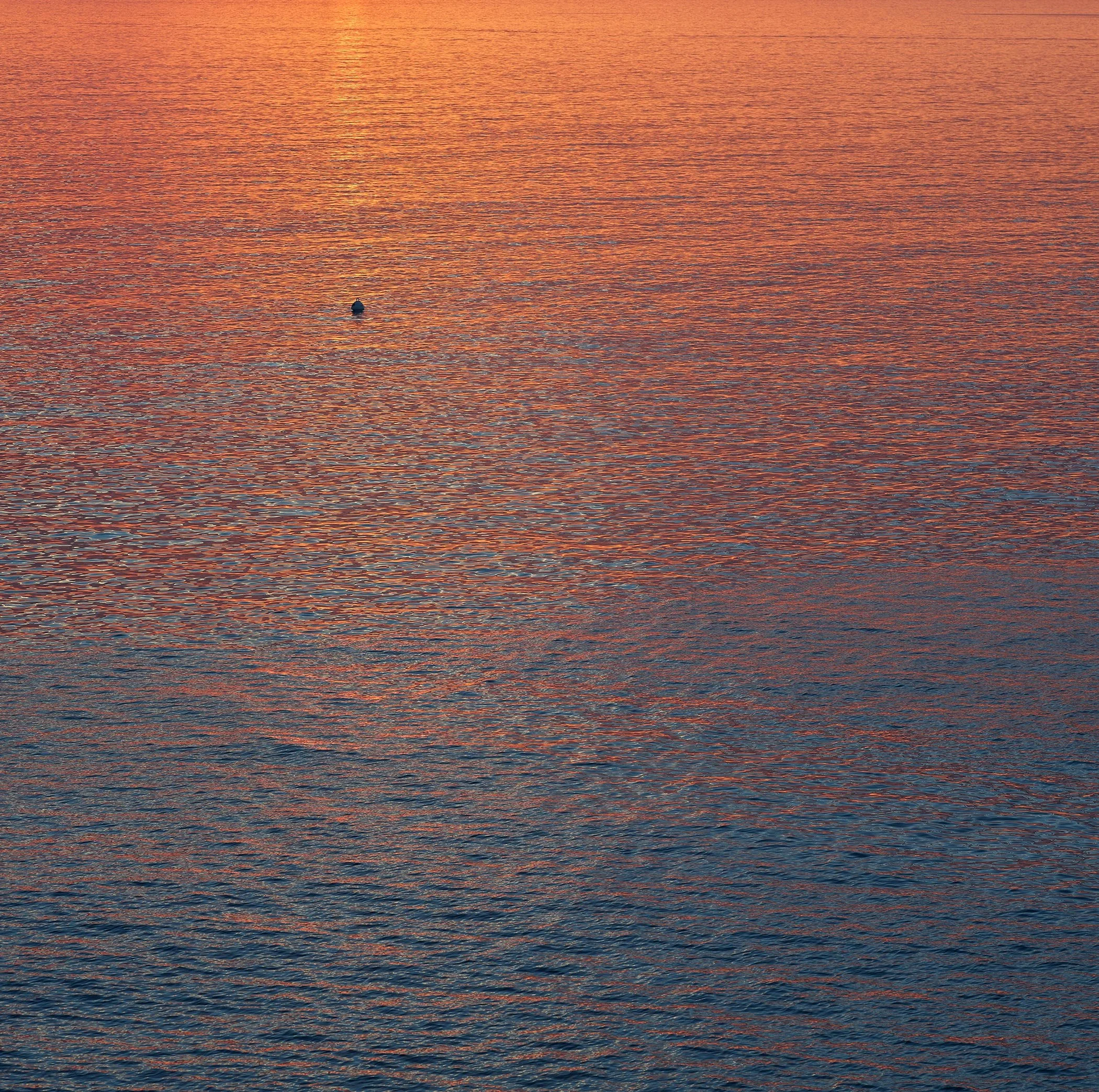 Coucher de soleil sur une mer calme avec une seule bouée flottante.