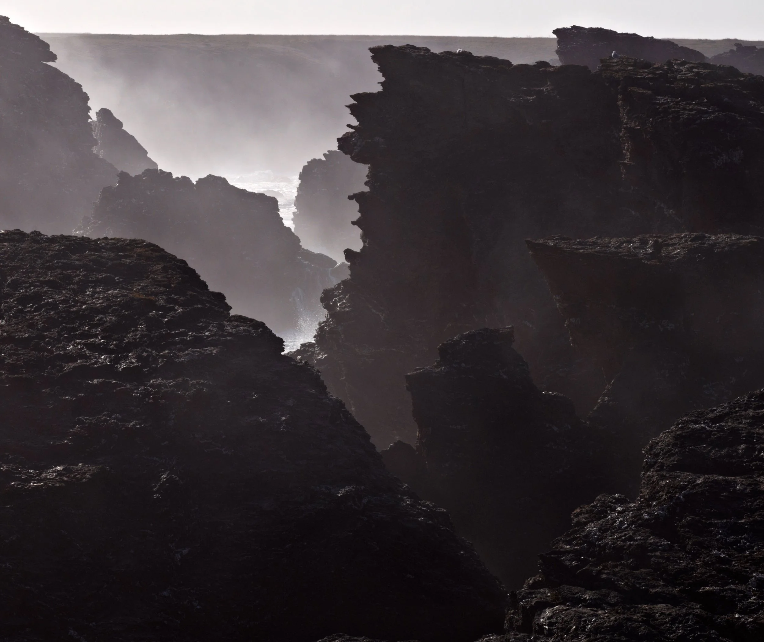 Des rochers noirs escarpés sur une plage rocheuse avec de la brume et des vagues d'eau.