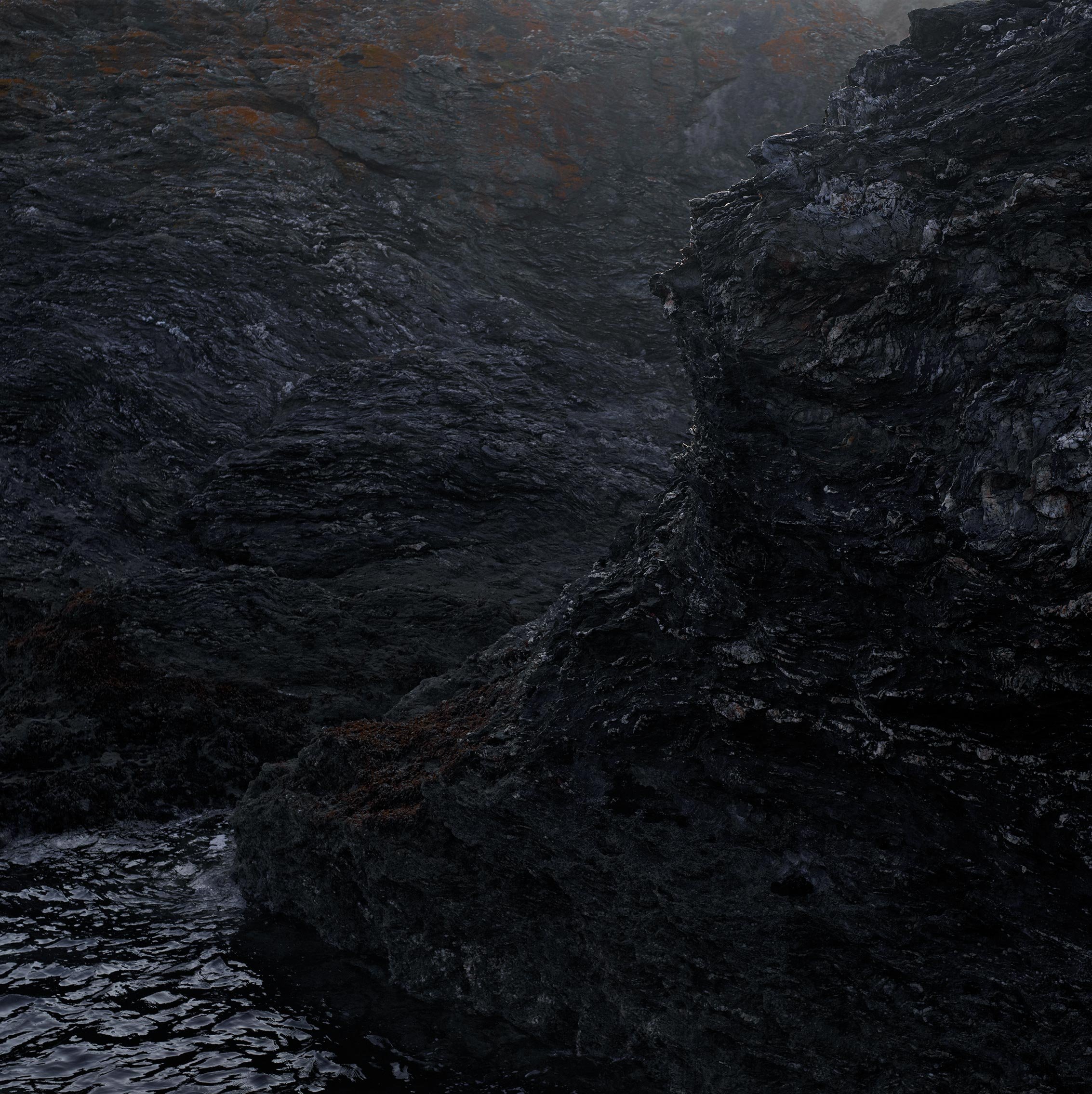 Une rivière ou un torrent avec des rochers sombres et humides, l'eau coule rapidement dans un paysage rocheux.