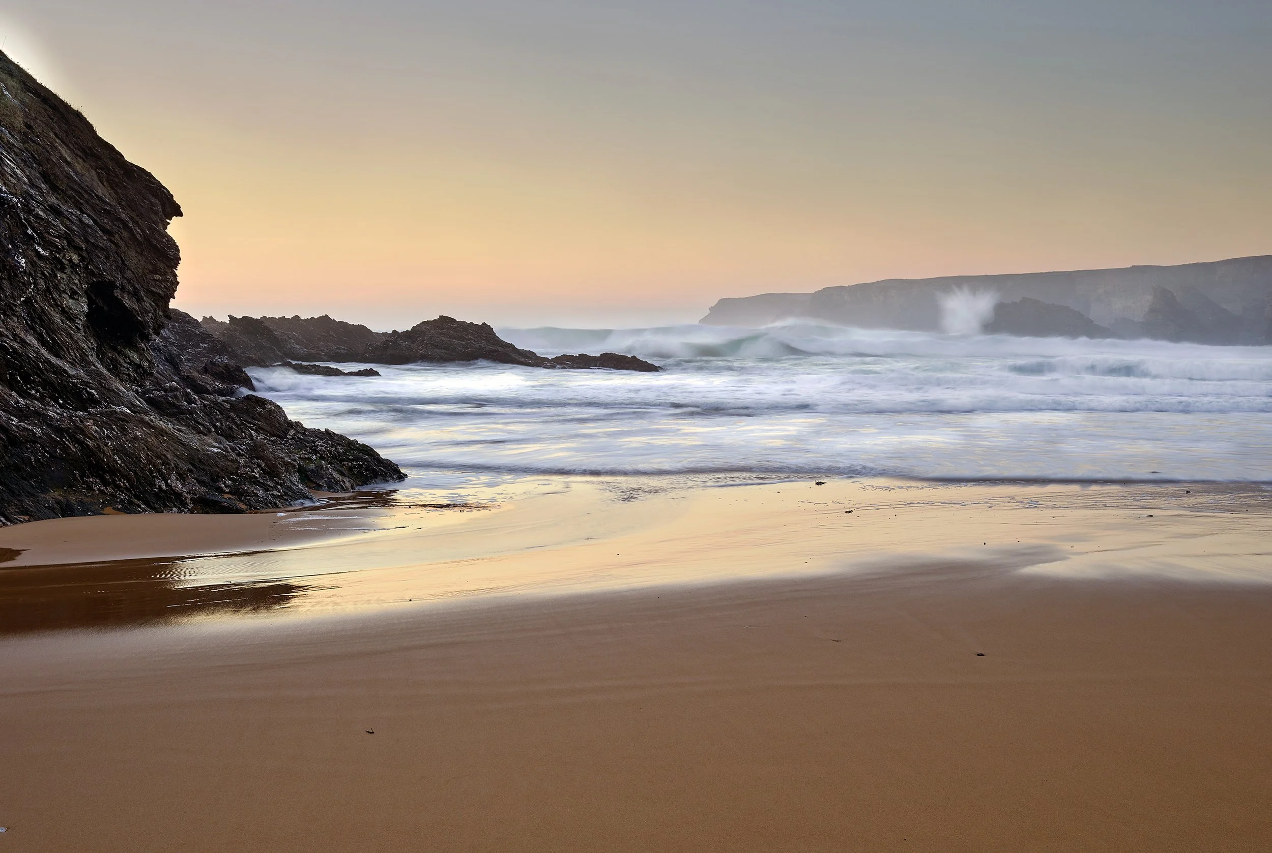 Plage de sable avec des vagues qui s'écrasent contre des rochers au coucher du soleil
