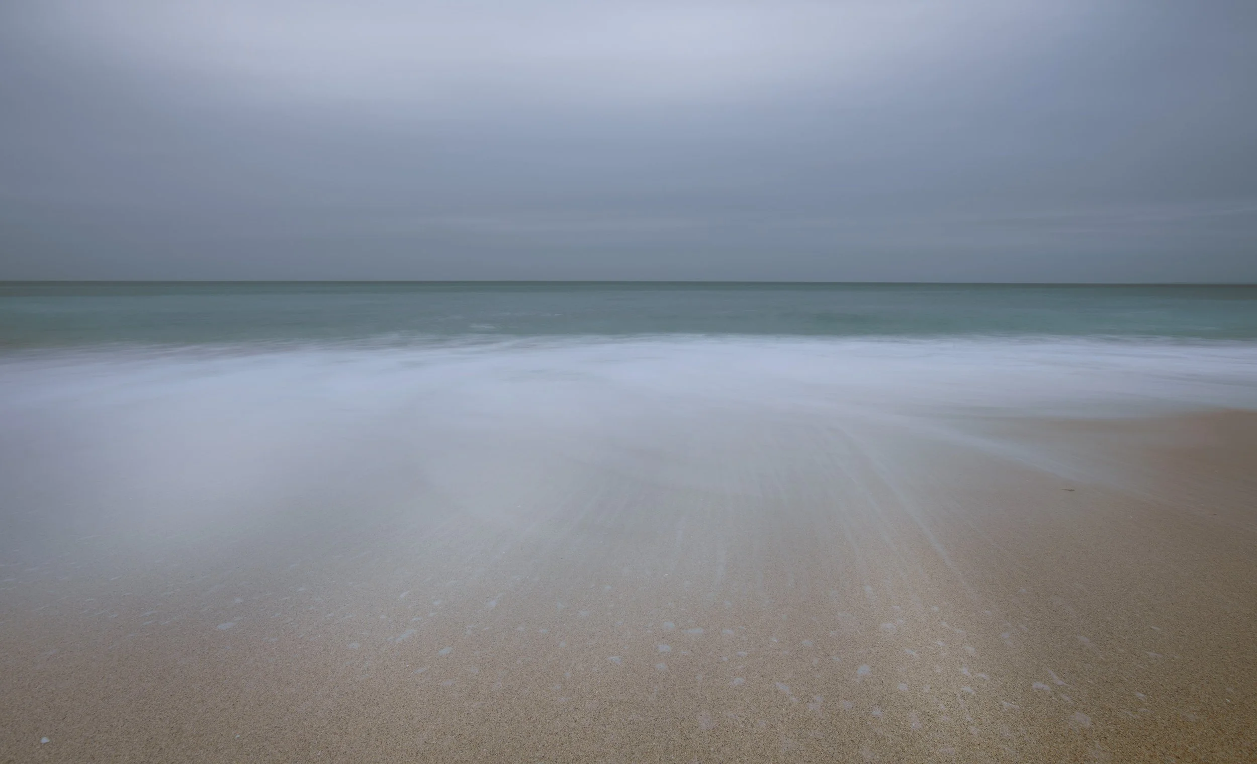 Plage de sable avec vagues calmes et ciel gris couverte de nuages