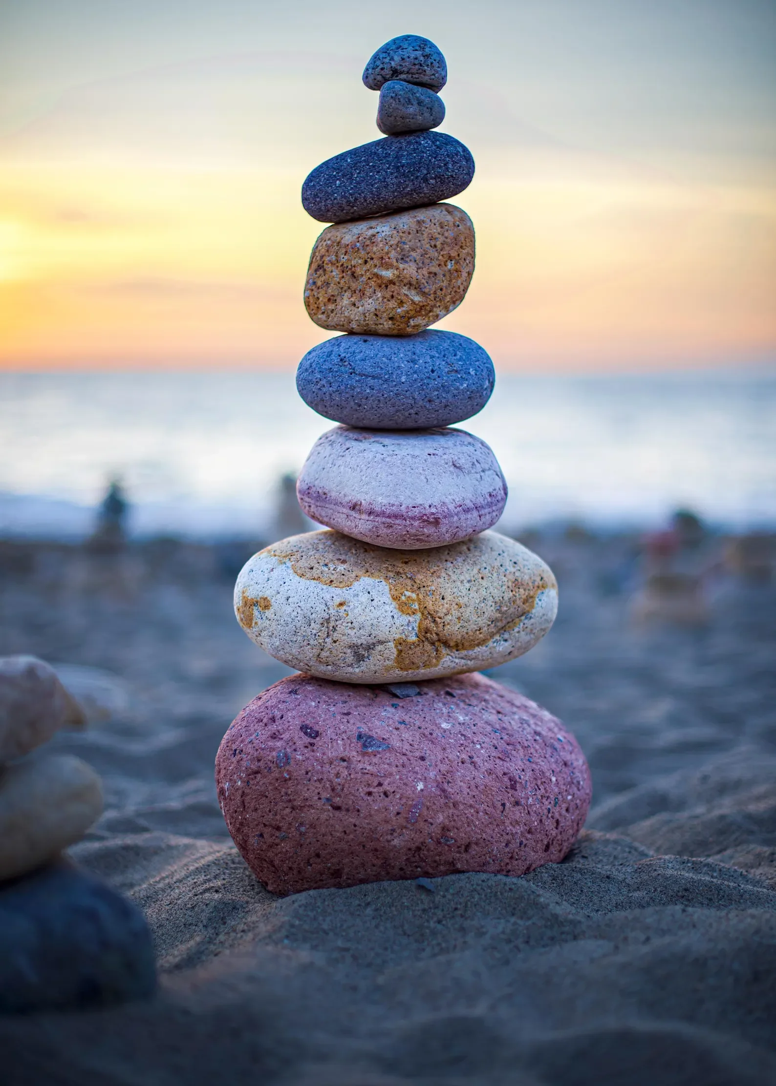 Stack of colorful stones balanced on a sandy beach at sunset