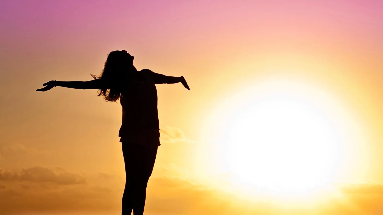 Silhouette of a woman with arms outstretched against a colorful sunset