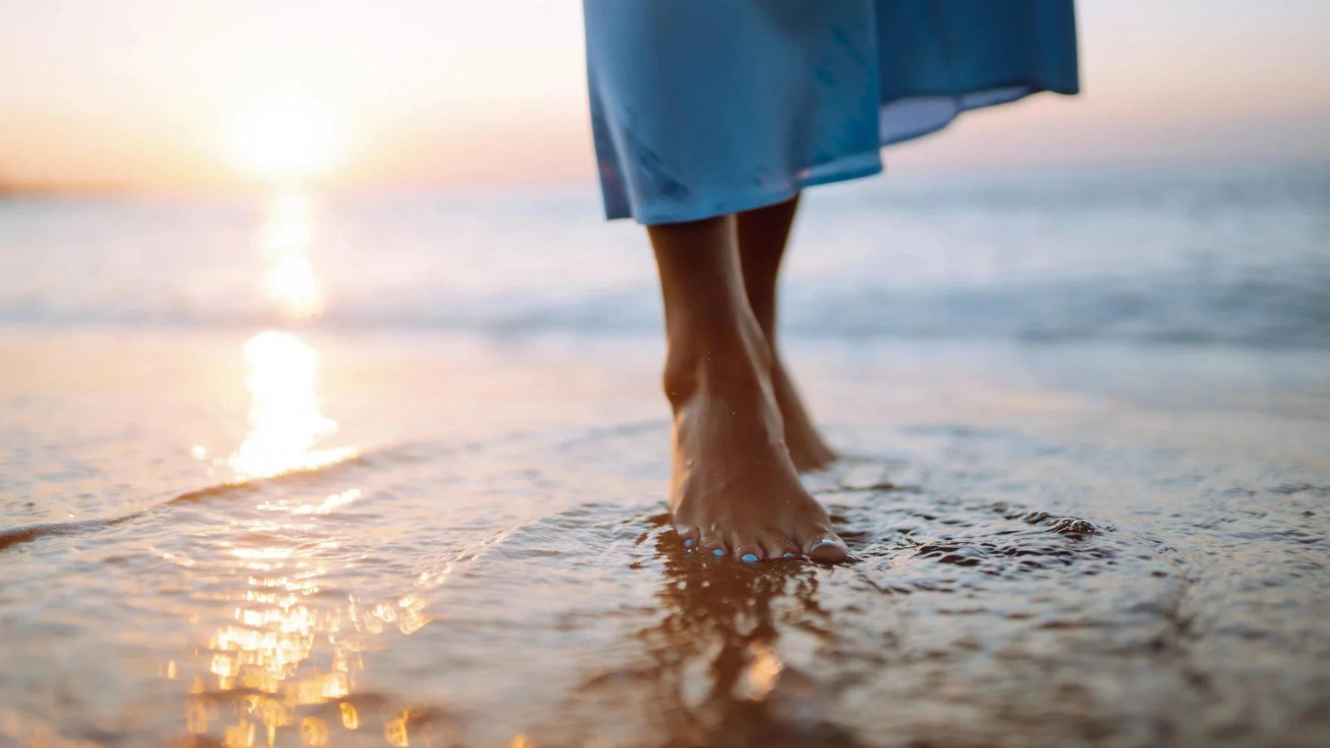 Bare feet walking on wet sand at the beach during sunset