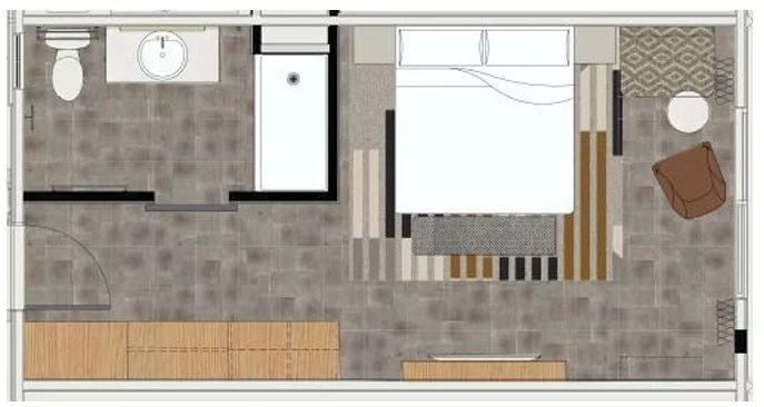 Top-down view of a bedroom with a bed, a small seating area with a brown chair and a round table, a bathroom with a toilet and sink, and a hallway with storage cabinets.