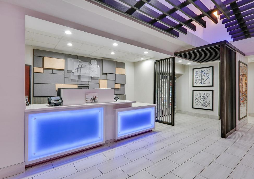 Modern hotel reception desk with blue illuminated panels, abstract wall art, and a decorative partition wall.