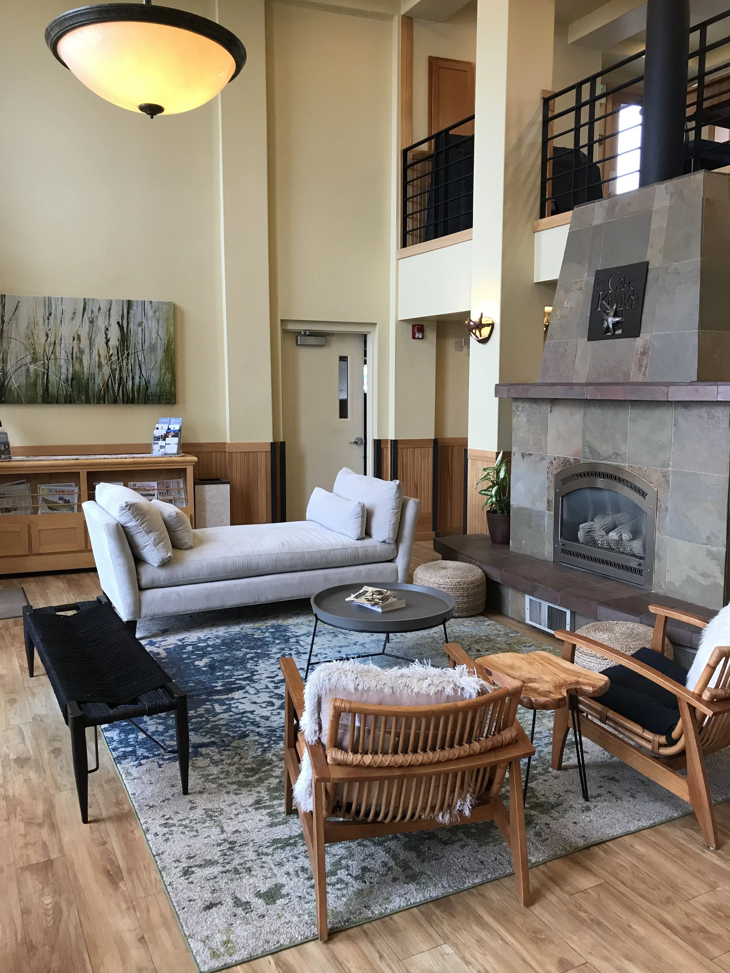 A cozy living room with white sofa, black armchairs, a round coffee table, wooden chairs with white fur, a fireplace, and a colorful area rug.
