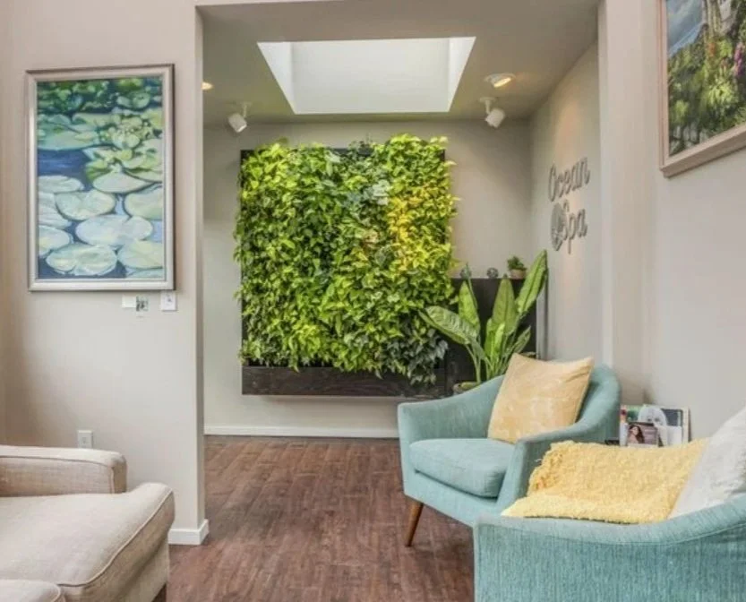 Living room with modern decor, featuring a large green plant wall, artwork, an outdoor sky view, and cozy seating with cushions.