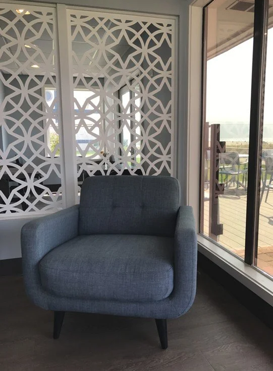 Gray armchair in a room with decorative white lattice divider and sliding glass door leading to an outdoor balcony with chairs.