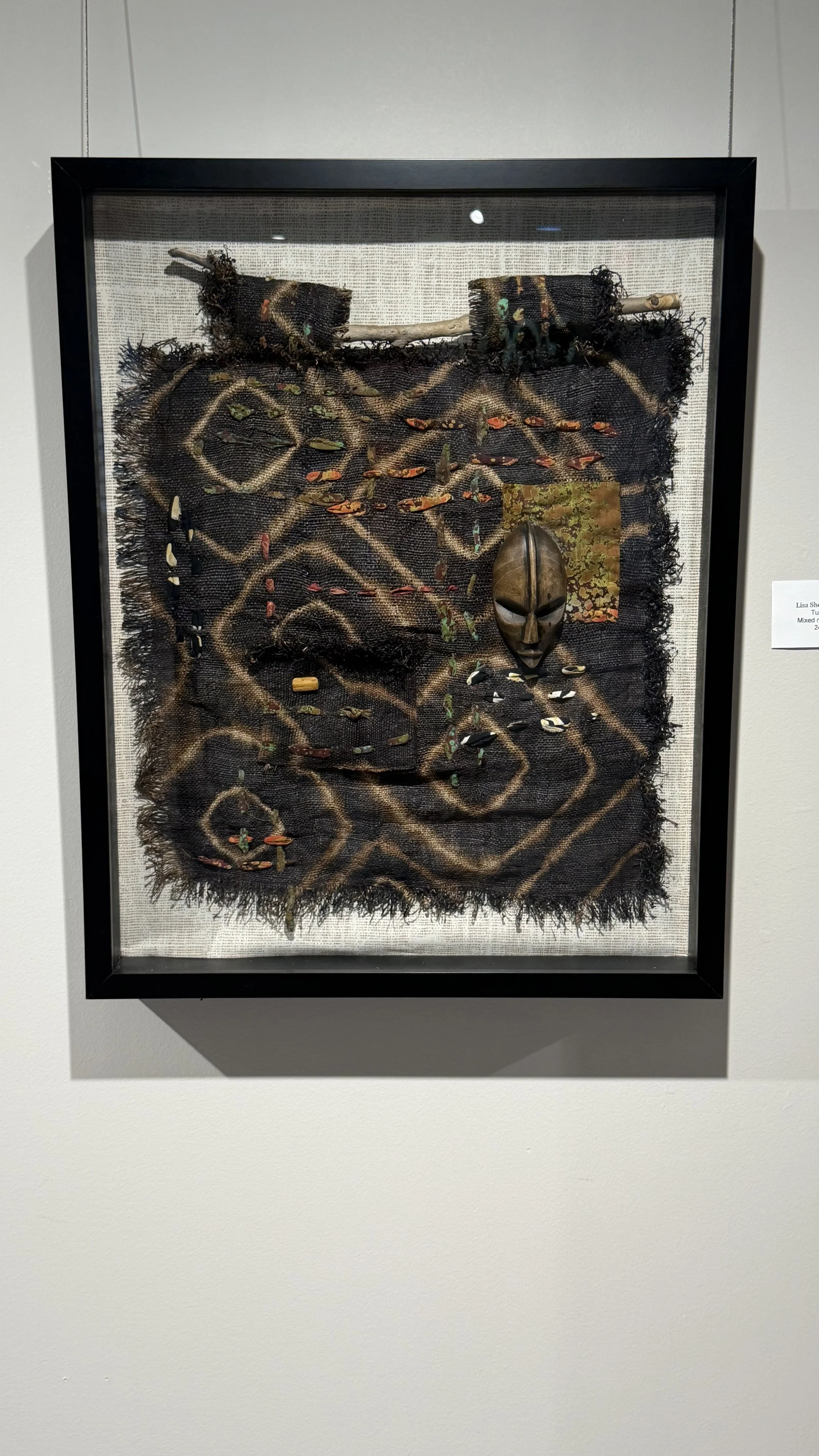 Mixed media art piece featuring a black fabric background with an African mask, small fish images, and various textures and patterns.