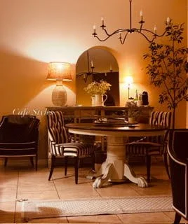 Dining room with a round table, four striped chairs, a large mirror, a chandelier, a table lamp, and a decorative plant.