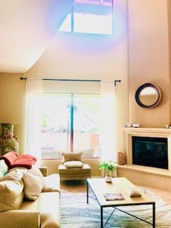 Living room with large window, beige couch, round mirror on wall, fireplace, and coffee table.