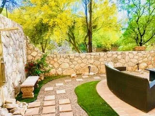 Outdoor patio with stone wall, curved pathway, green grass, and trees in the background.