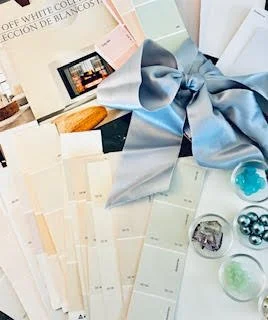 Color palette and swatches with a large blue satin bow on top, surrounded by paint samples and decorative objects.