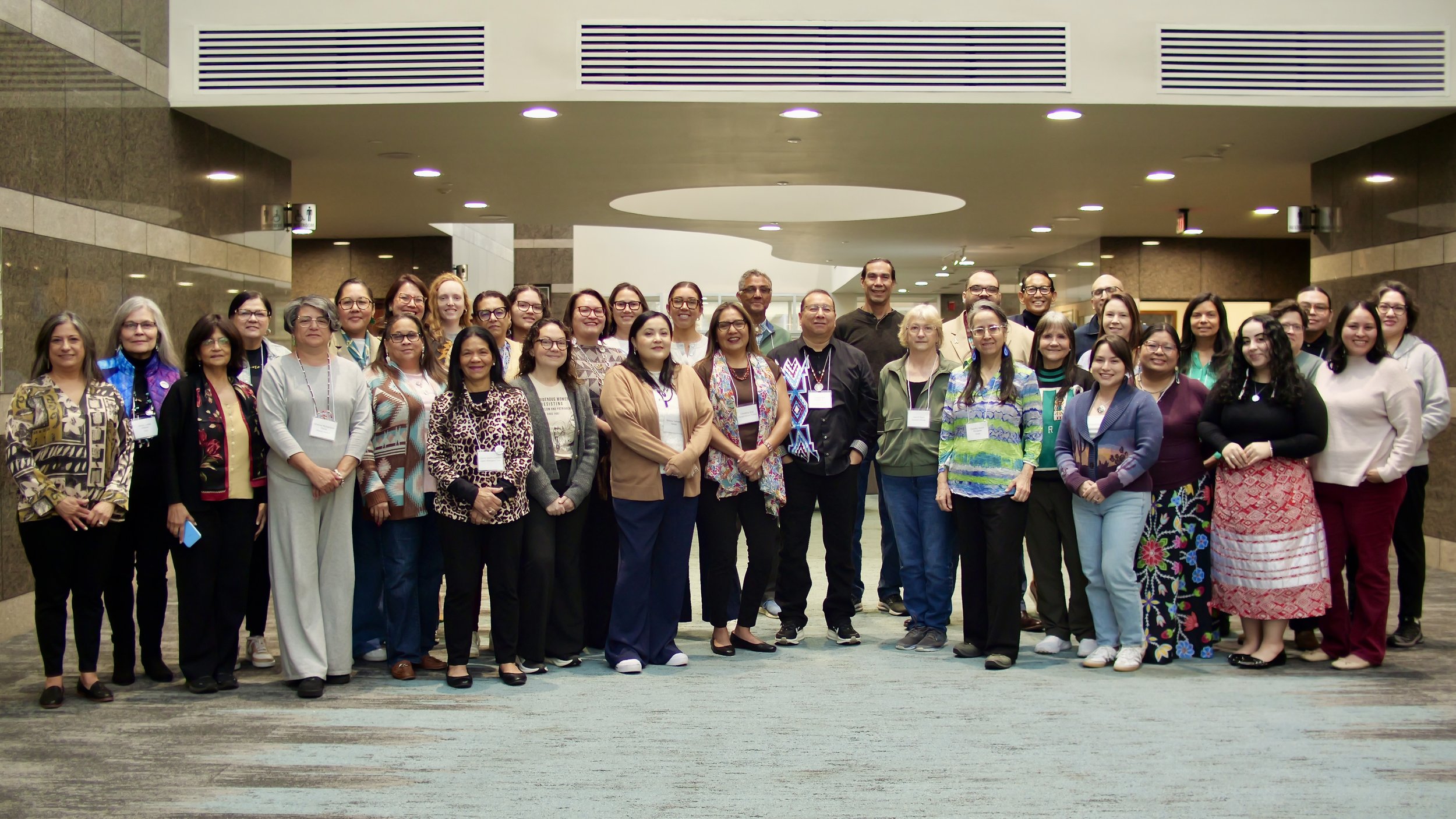 Group of diverse women and men standing together in a lobby, smiling for the photo, at the AIANNH Cancer Consortium.