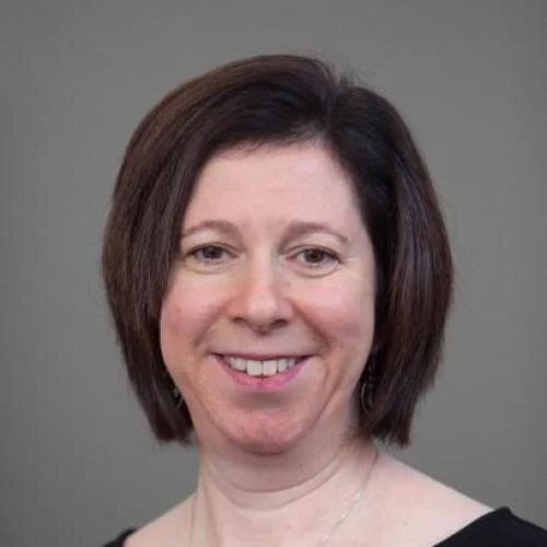 A photo of Jennifer Freedman, PhD, with short, dark brown hair smiling at the camera against a plain gray background.
