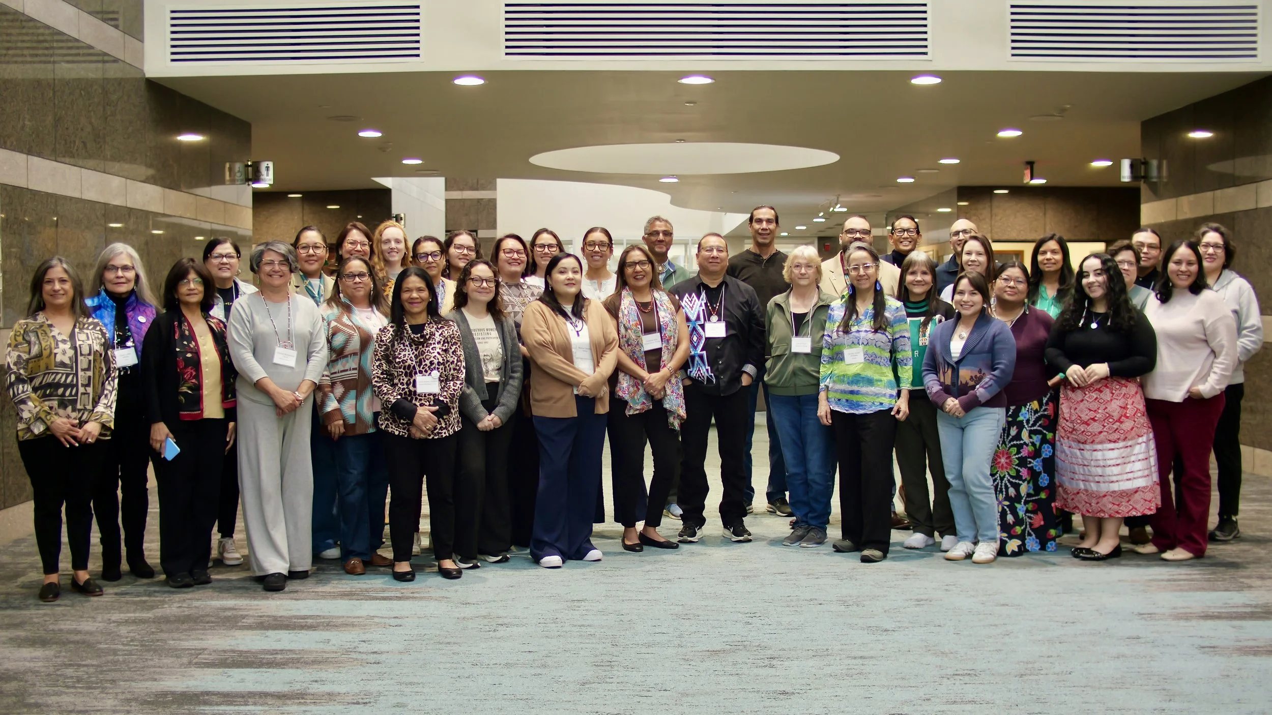 Group of diverse people standing together in an indoor setting, smiling at the camera.