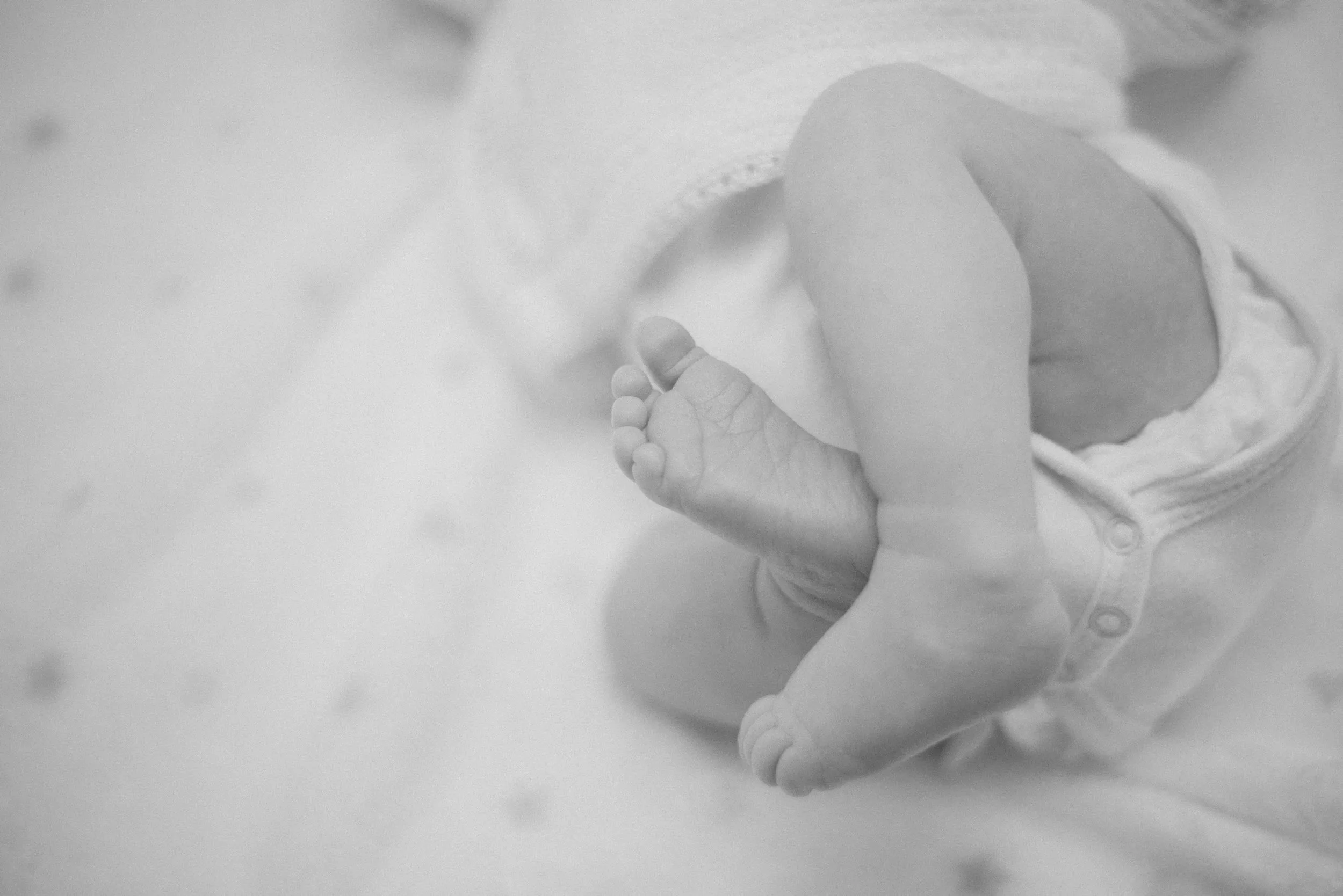 Black and white photo of a baby holding an adult's hand.