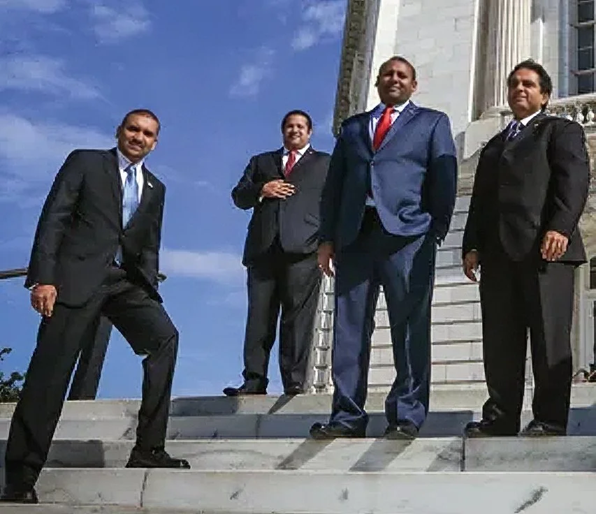 Four men of AAHOA in suits standing on steps outside a government or official building.