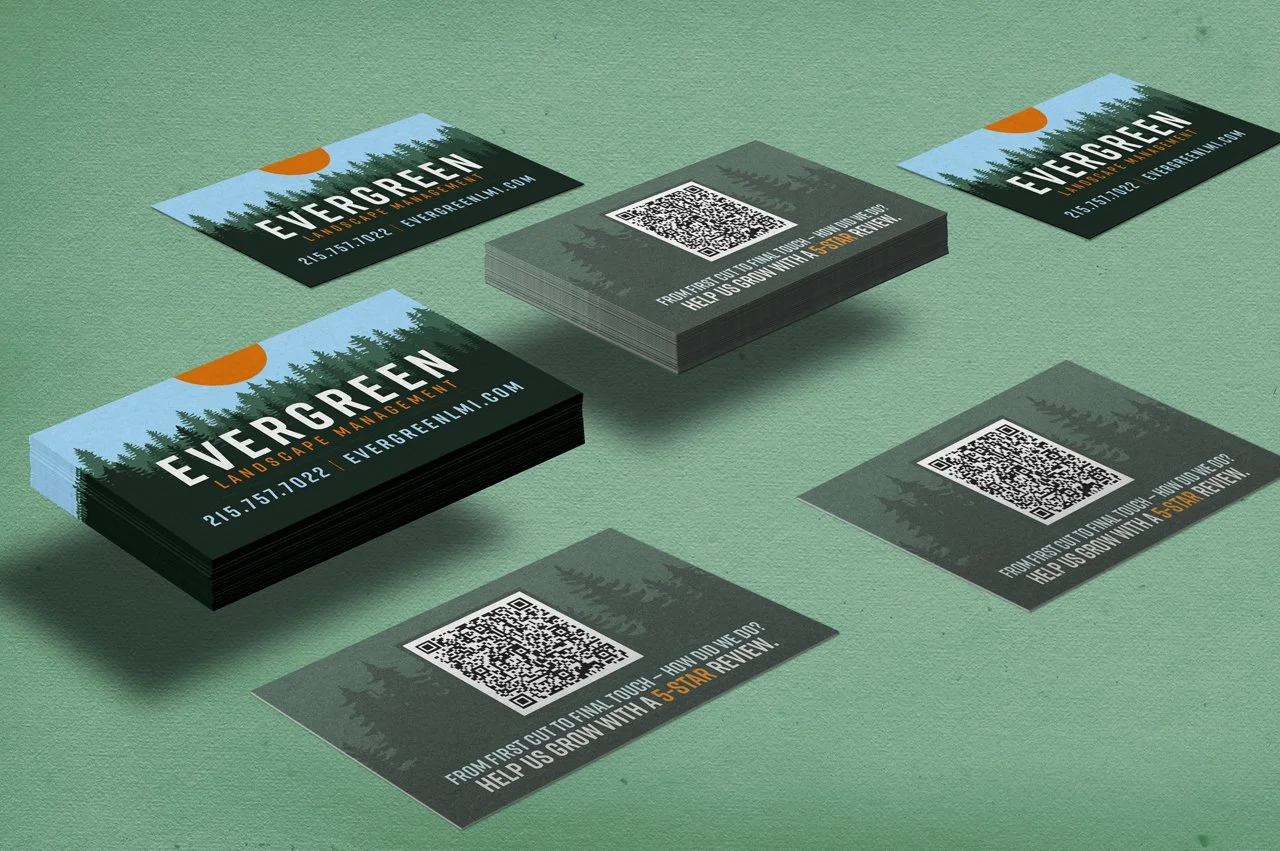 Stack of business cards and two flyer cards on a green surface promoting Evergreen Landcape Management with a mountain and tree forest background and a setting sun, along with QR codes and review request message.