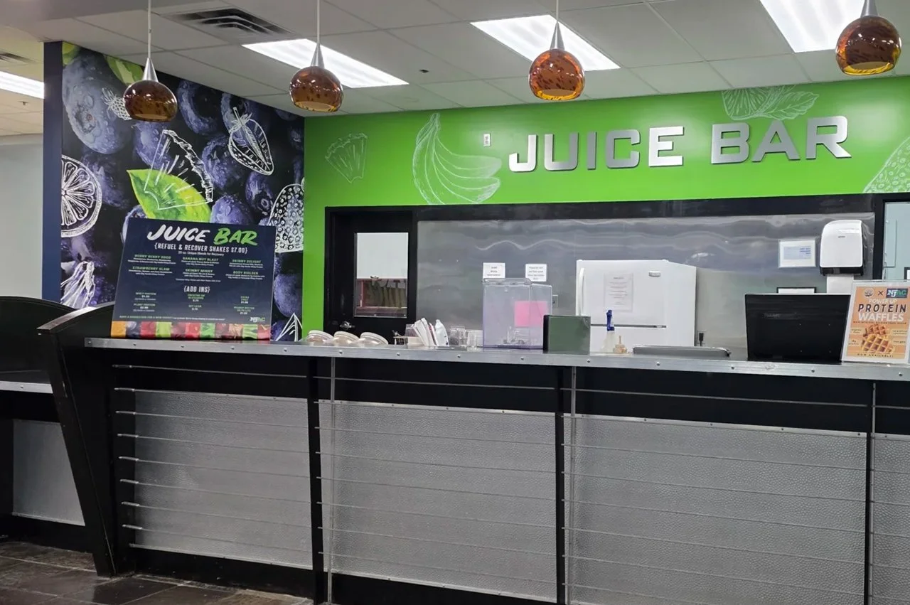 NJAC Juice bar counter inside a juice shop with a green wall, large 'JUICE BAR' sign, and menu board.