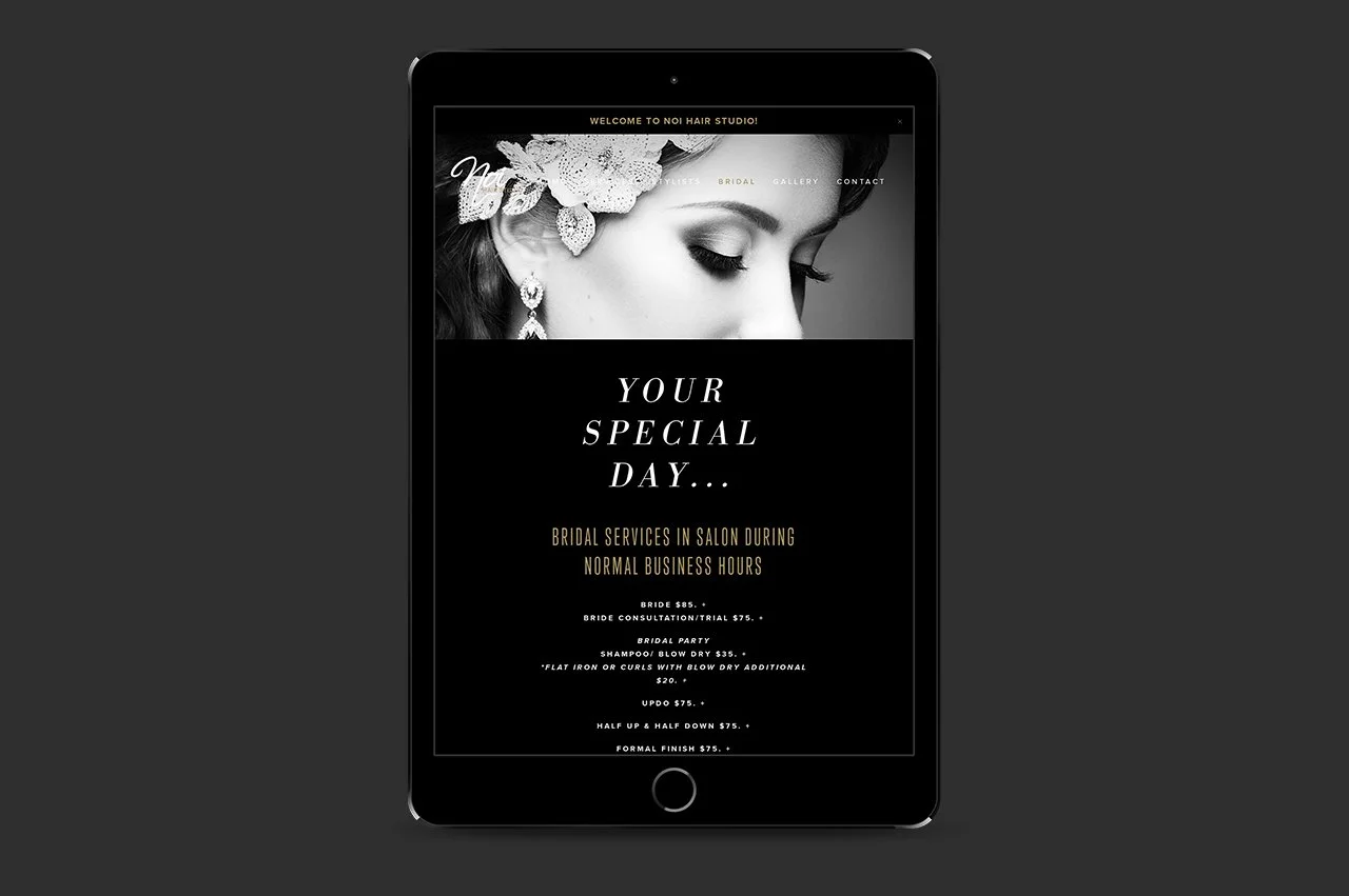 A tablet displaying a black and white Noi  Hair Studio webpage, featuring a close-up of a woman's face with a floral headpiece, promotional text about bridal services, and a menu of salon packages.