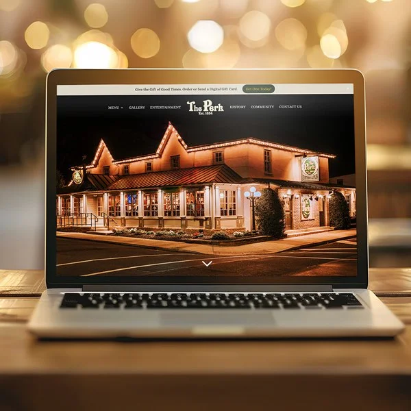 Laptop displaying 'The Park' restaurant website, showcasing an outdoor evening patio layout.