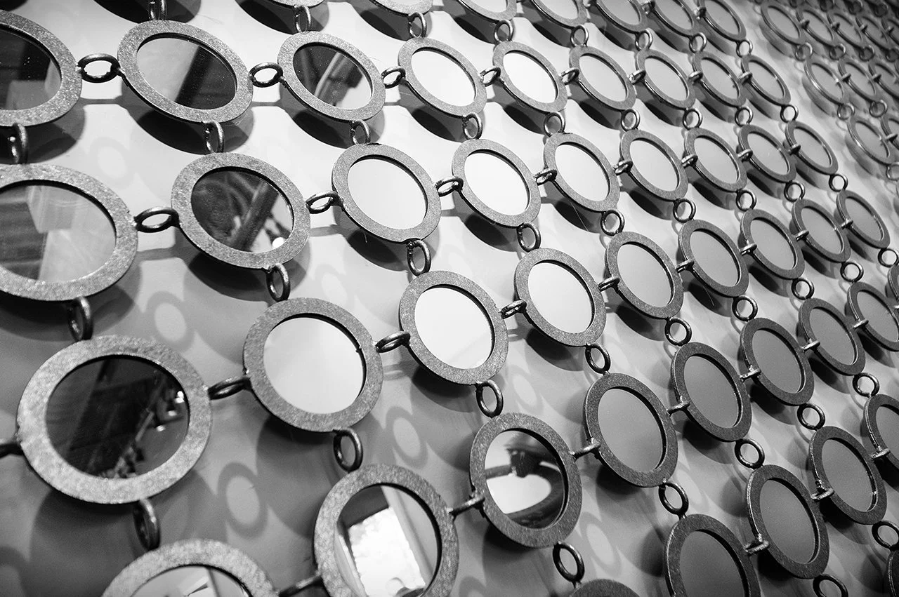 Multiple circular mirrors with metal borders hanging in a grid pattern on a wall.