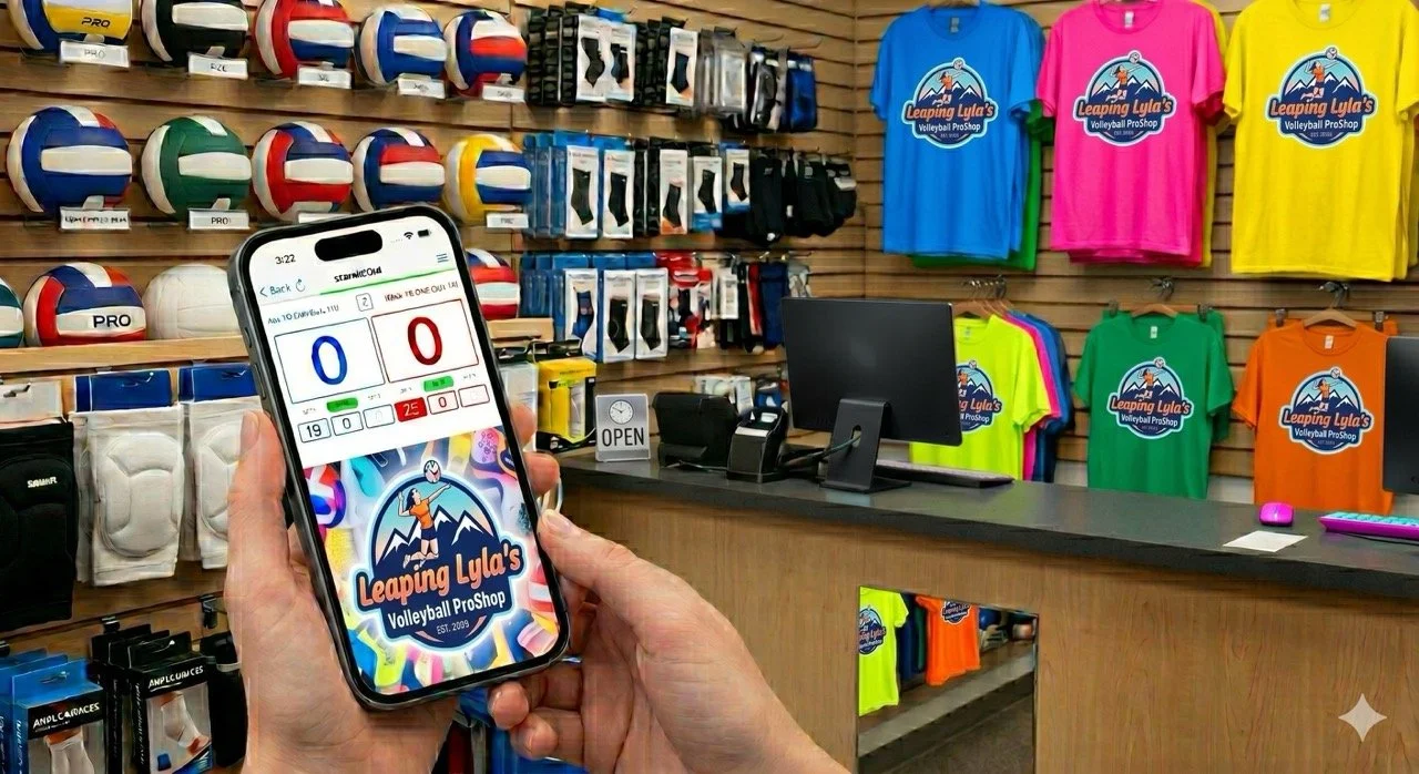 Mobile phone displaying a volleyball score app, held in front of a sports store with volleyballs, knee pads, and colorful t-shirts on the wall showing "Leaping Lyla's Volleyball ProShop" logo.