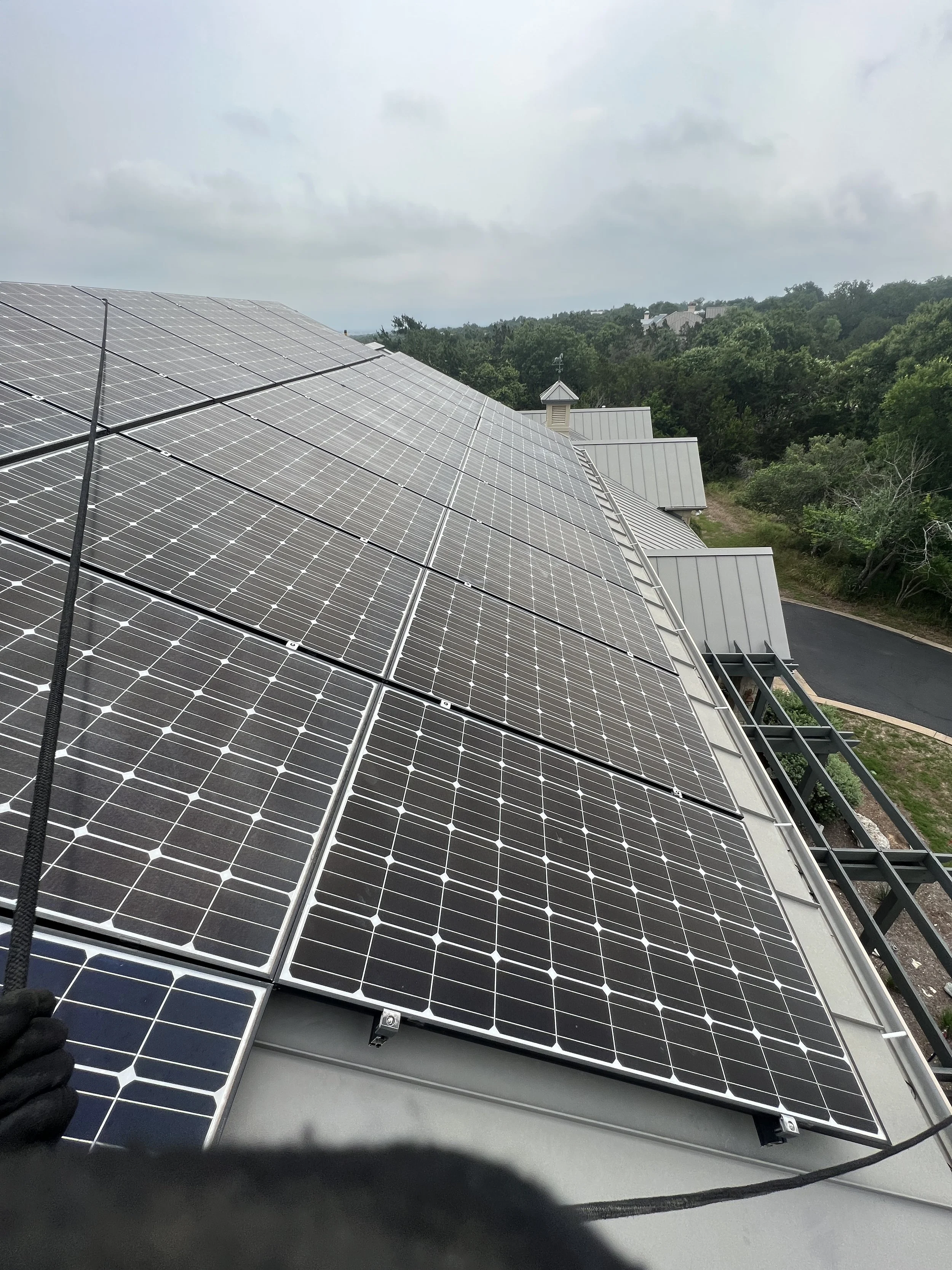 Close-up view of solar panels installed on a roof with cloudy sky and trees in the background.