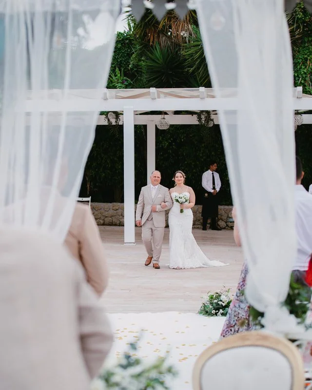Bride walking down the aisle with her father at an outdoor wedding ceremony.