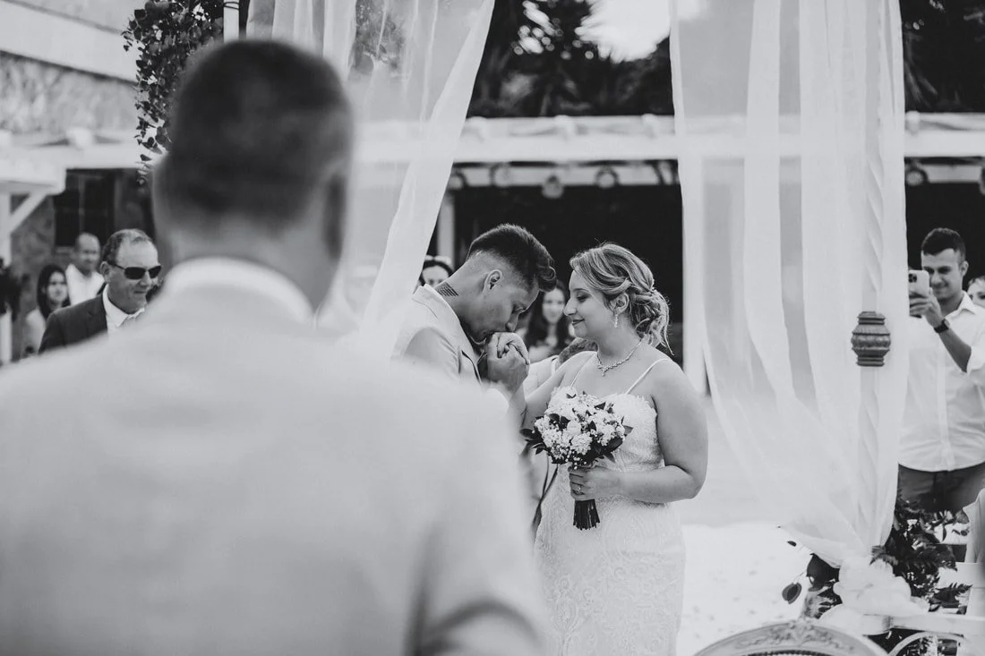 Black and white photo of a wedding ceremony with a bride and groom exchanging vows surrounded by guests.