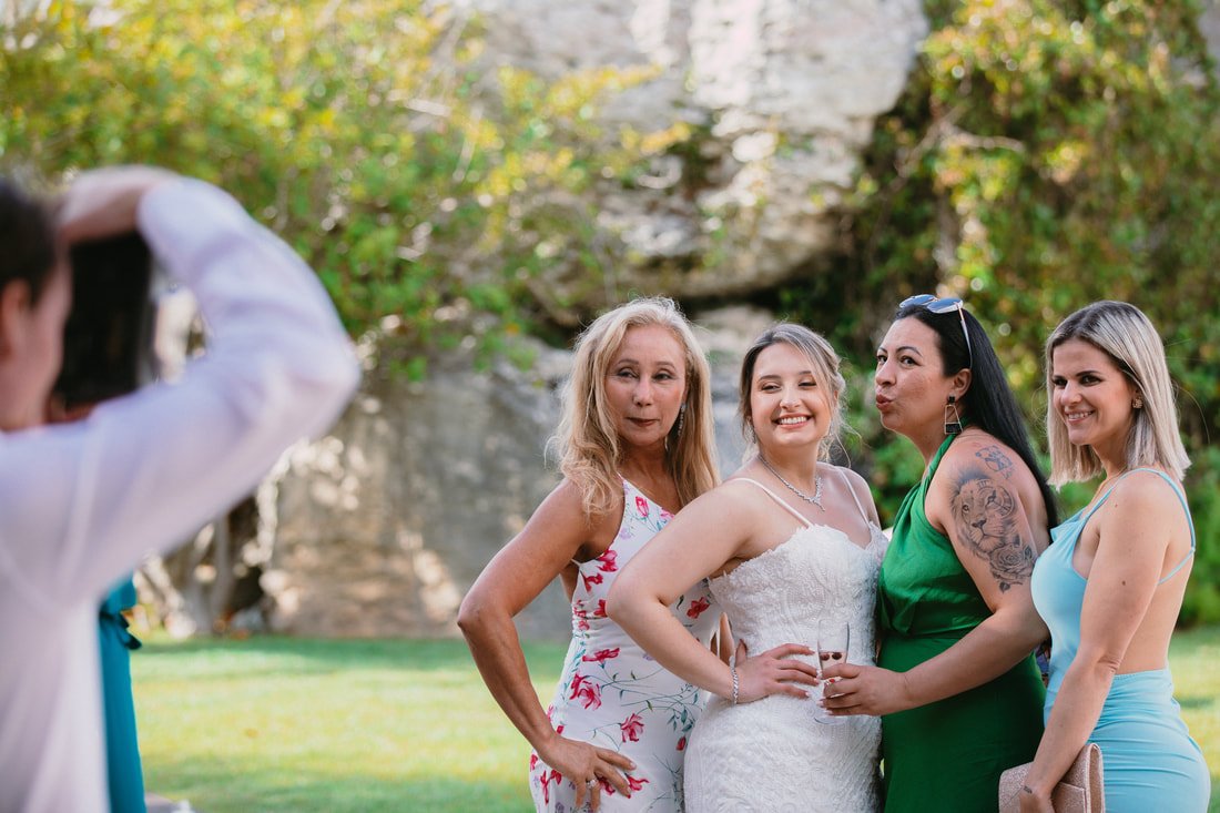 Group of four women posing for a photo outdoors in a natural setting during daytime, with a person taking the picture.