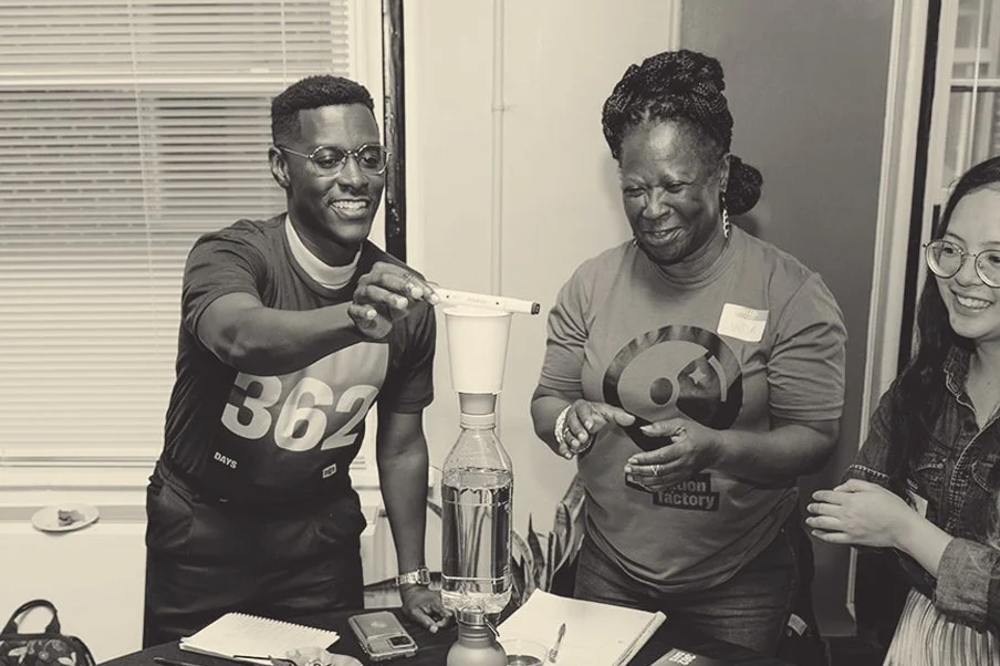 Three people participating in a science experiment with a paper funnel and a plastic bottle, in an indoor setting.