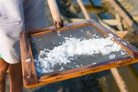 Person holding a wooden framed tray filled with crushed ice over a body of water.