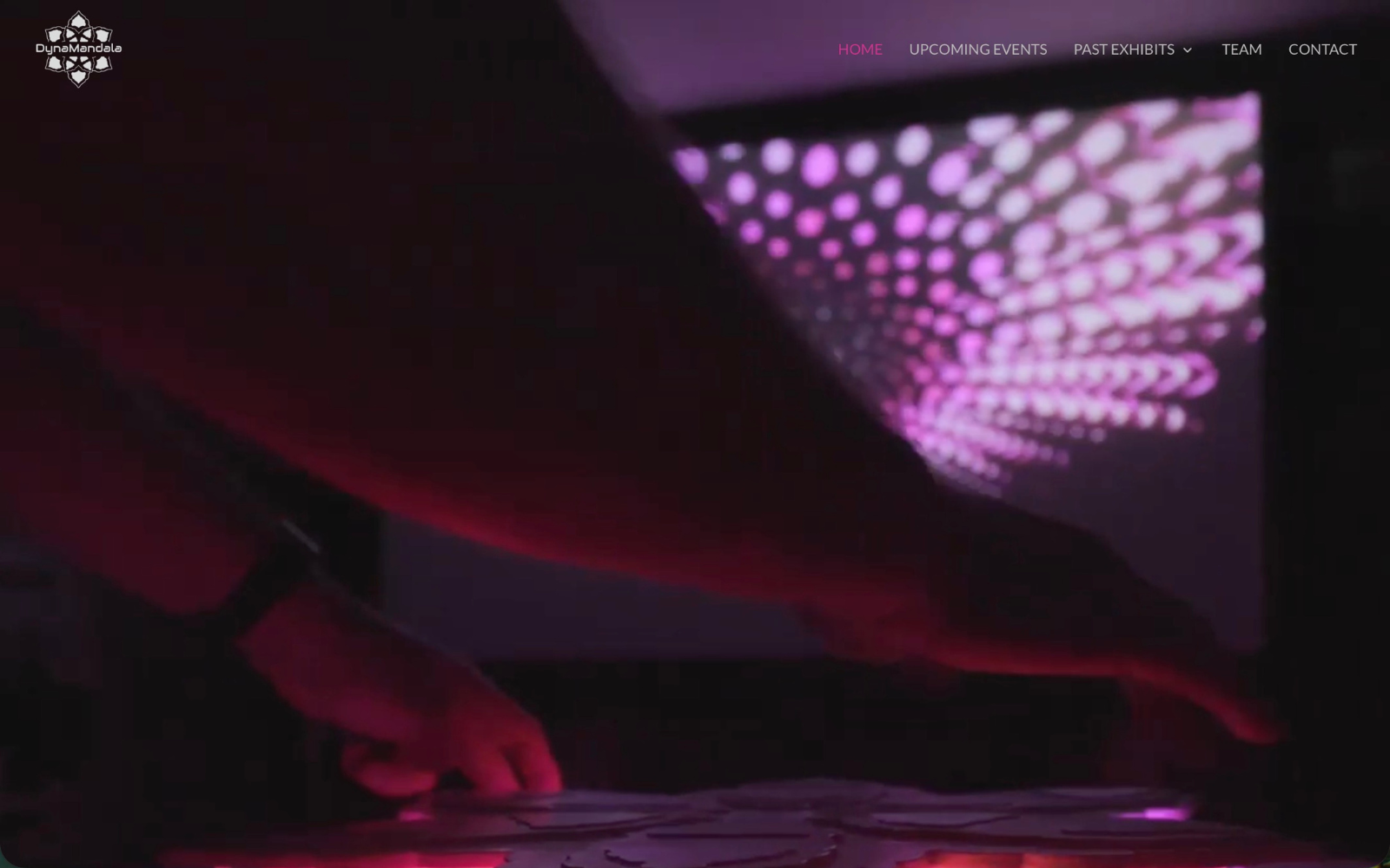 A still shot of a person using the Dynamandala interactive art console with pink and purple lights on a computer screen in front of them.