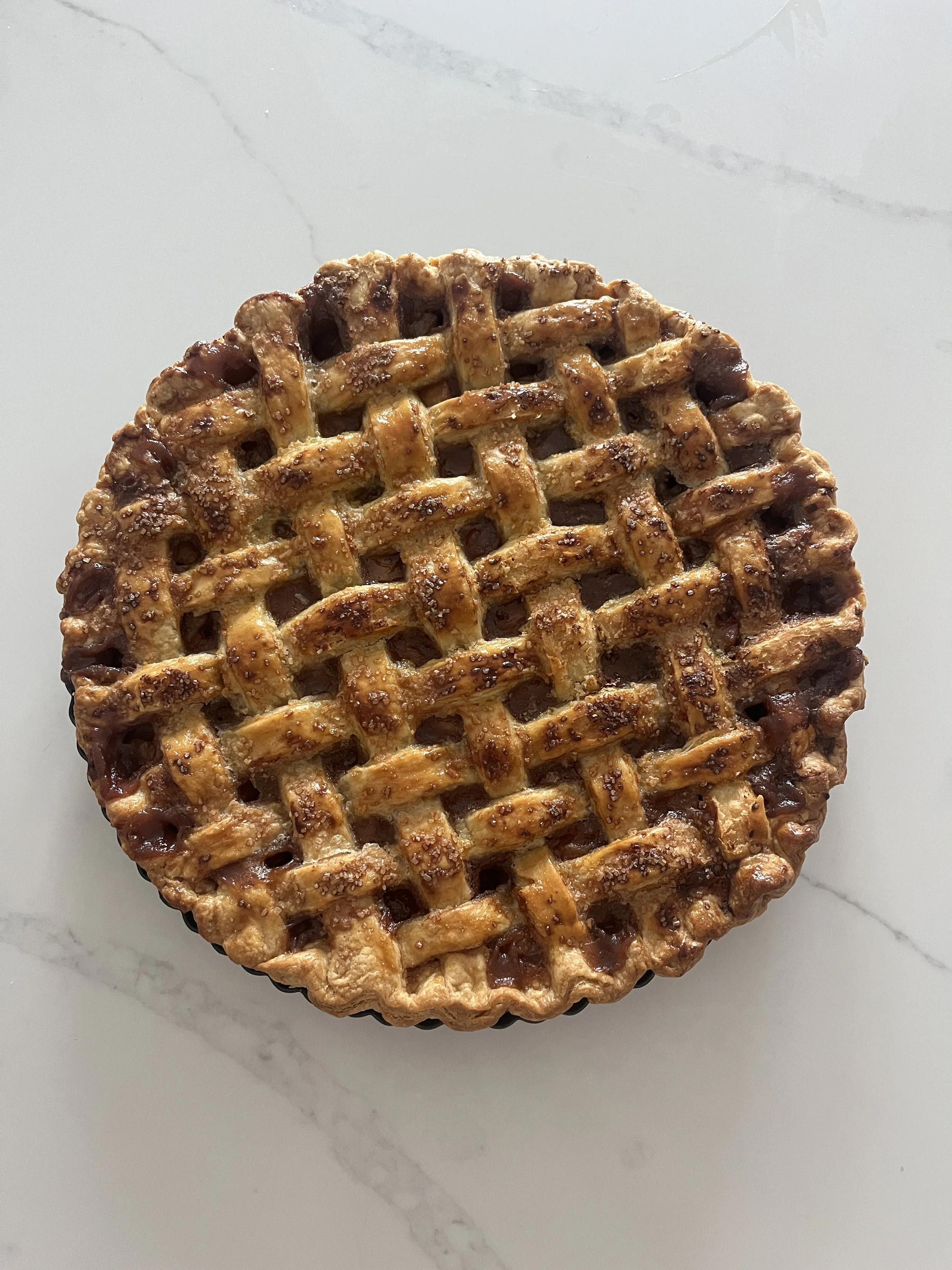 Close-up of a lattice-topped cherry pie on a white marble surface.